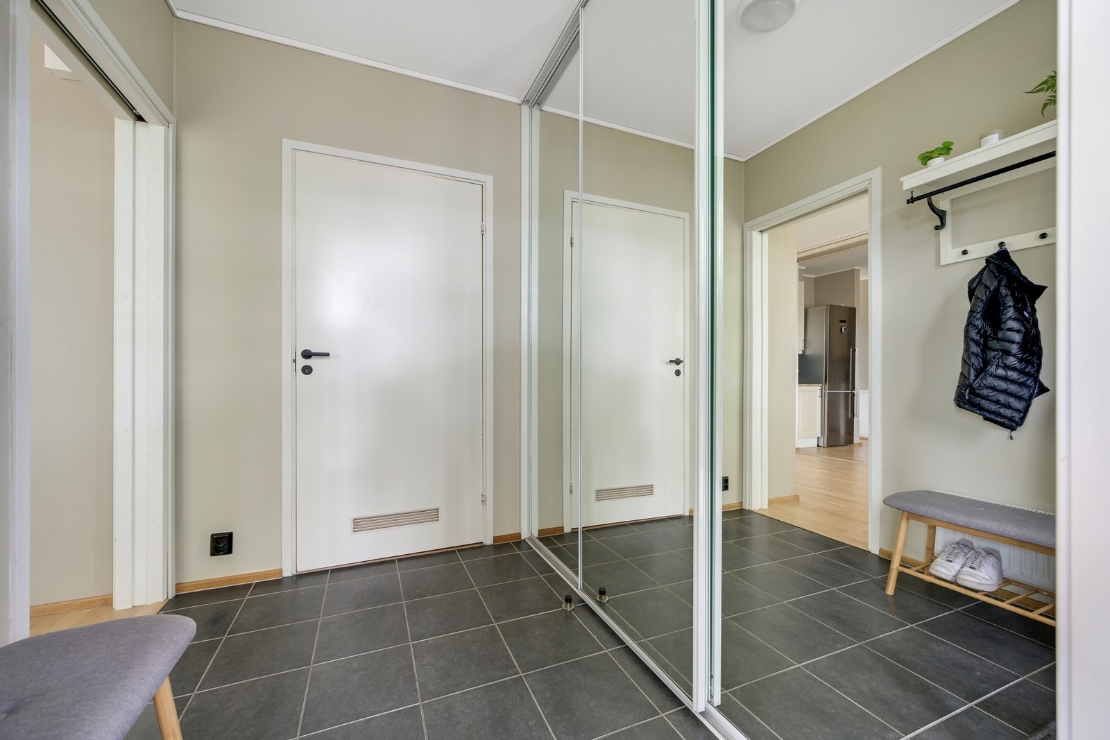 Velkommen inn i en innbydende og lys entré med flislagt gulv og malte vegger og tak. En praktisk skyvedørsgarderobe sørger for klesoppbevaringen. Galleribilde