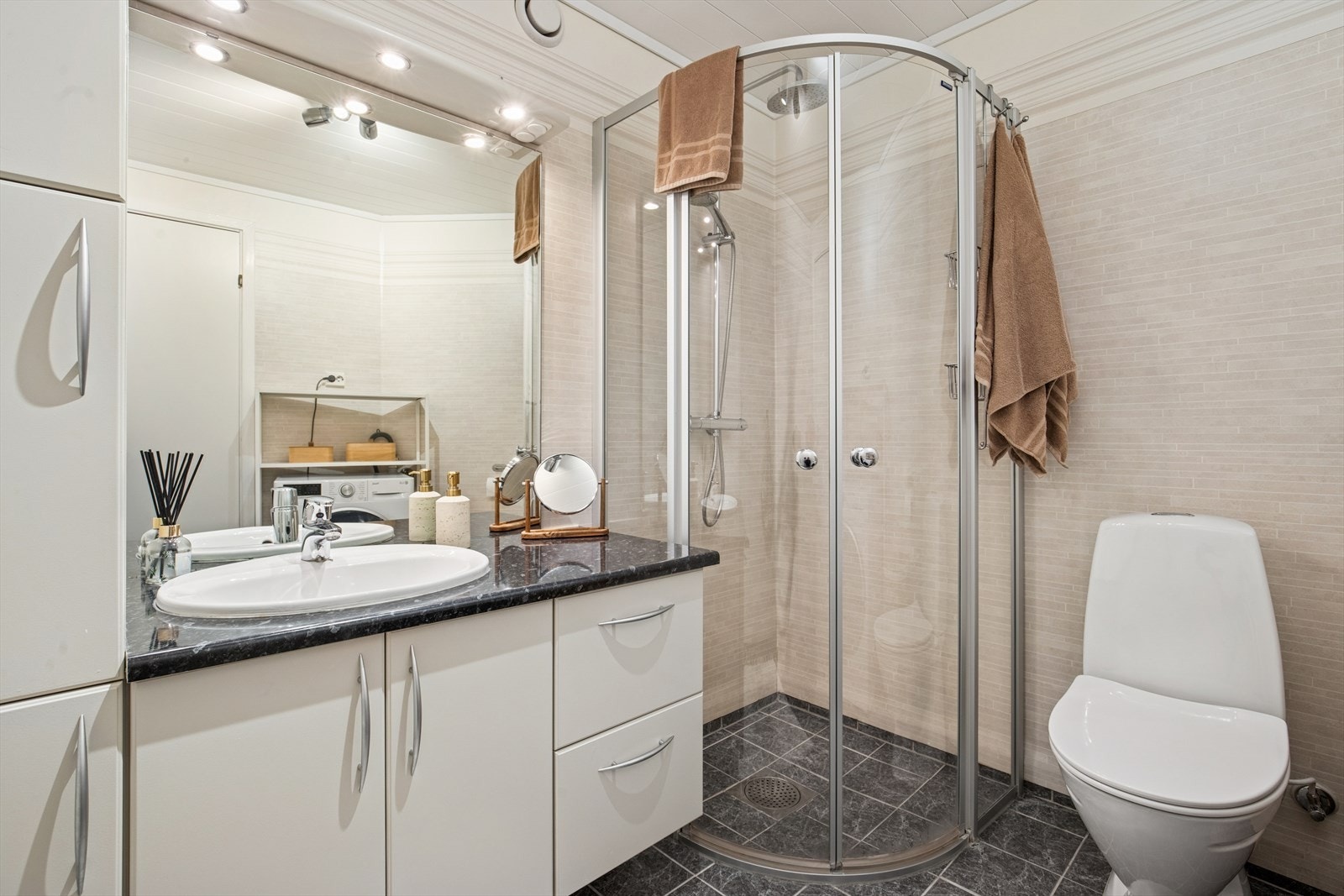 Badet består av speil, servant med oppbevaringsseksjon, toalett, dusj og opplegg for vaskemaskin. Galleribilde