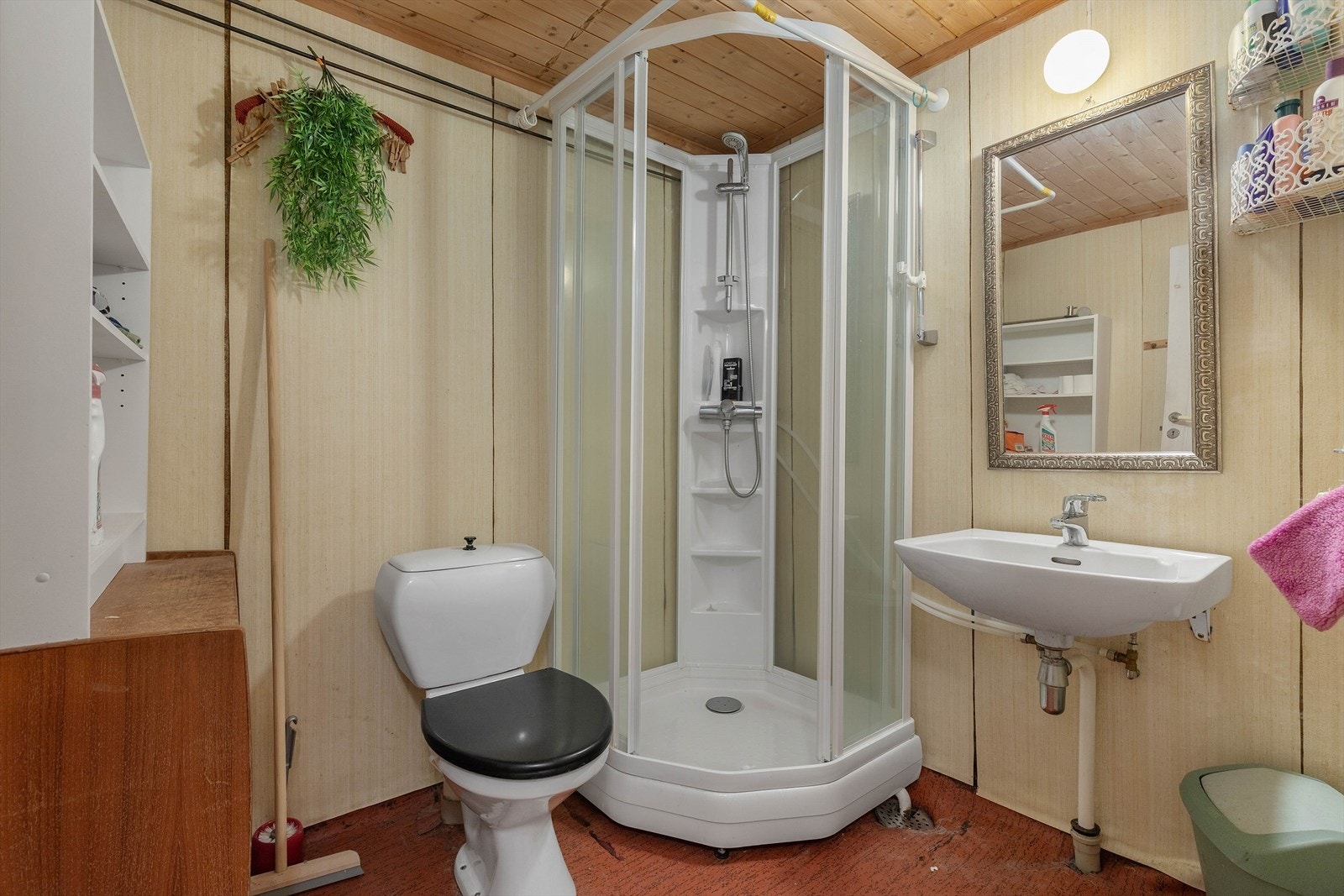 Eldre bad i kjeller, belegg på golv, plater på vegger og panel i himling. Her er det toalett, dusjkabinett og servant med spegel Galleribilde