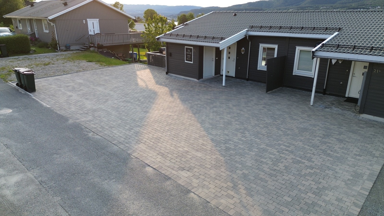 Stor steinlagt gårdsplass med plass til parkering. Elbil-lader ble installert på husveggen i 2025. Galleribilde