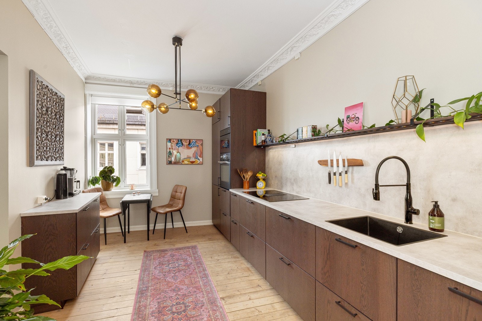 Integrert kjøleskap med frysedel, komfyr og mikrobølgeovn i høyskap, oppvaskmaskin i benk og nedfelt platetopp med innebygget ventilator. Galleribilde