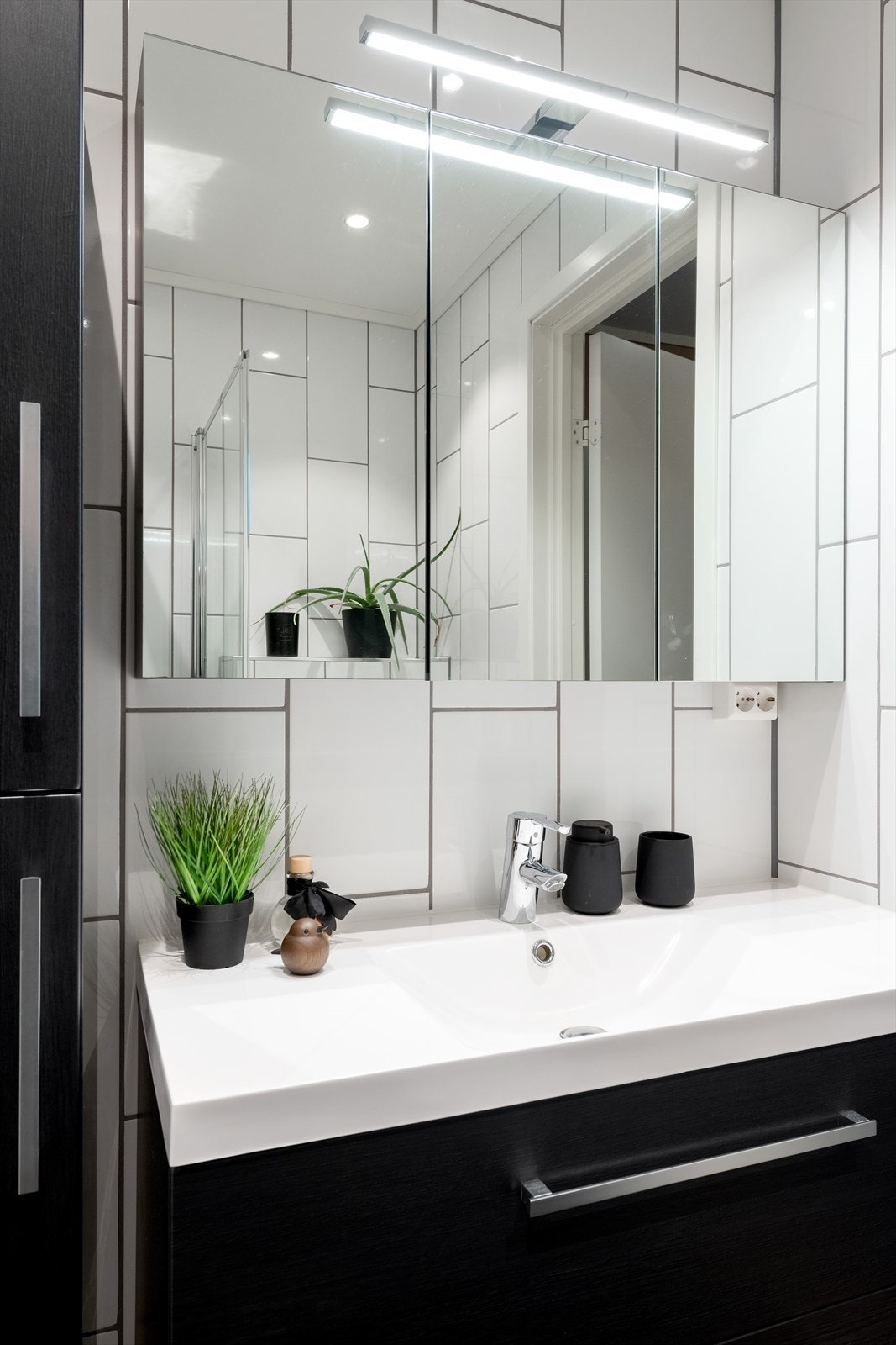 Sort badersomsinnredning med skuffer og skap og ovenpåliggende servant med ett-greps armatur. Speilskap med overlys og stikkontakt over servant. Galleribilde