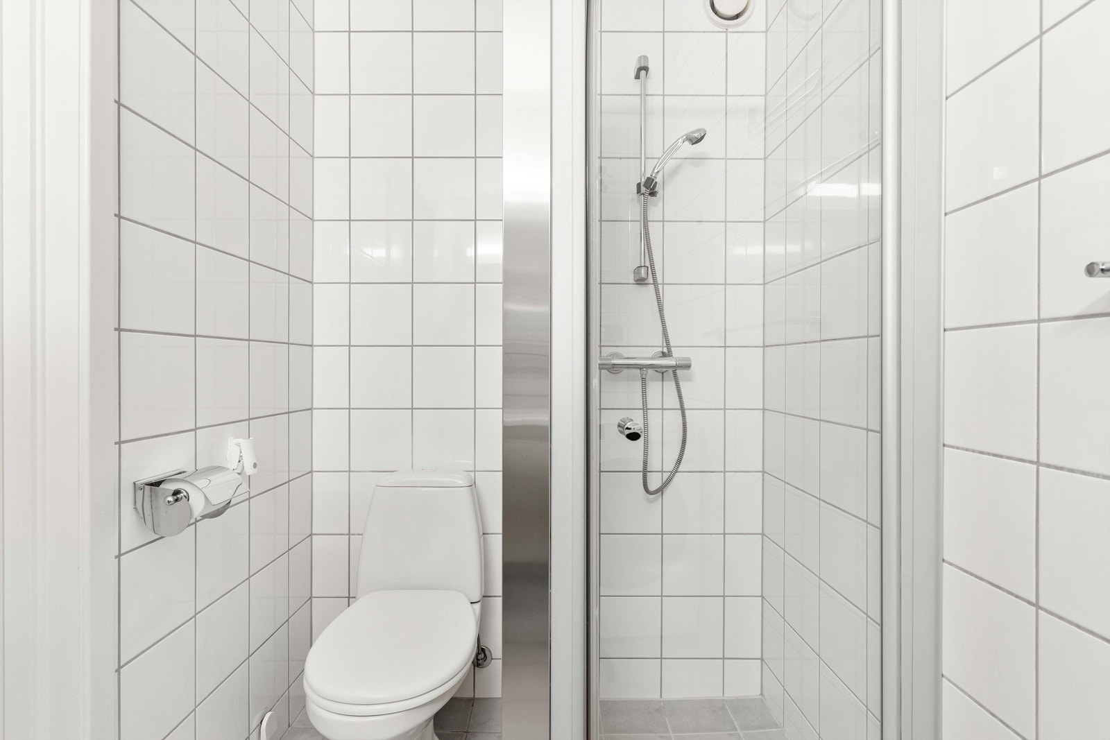 Dusjhjørne med innfellbar glassdør og dusjarmatur og et gulvmontert klosett. Galleribilde