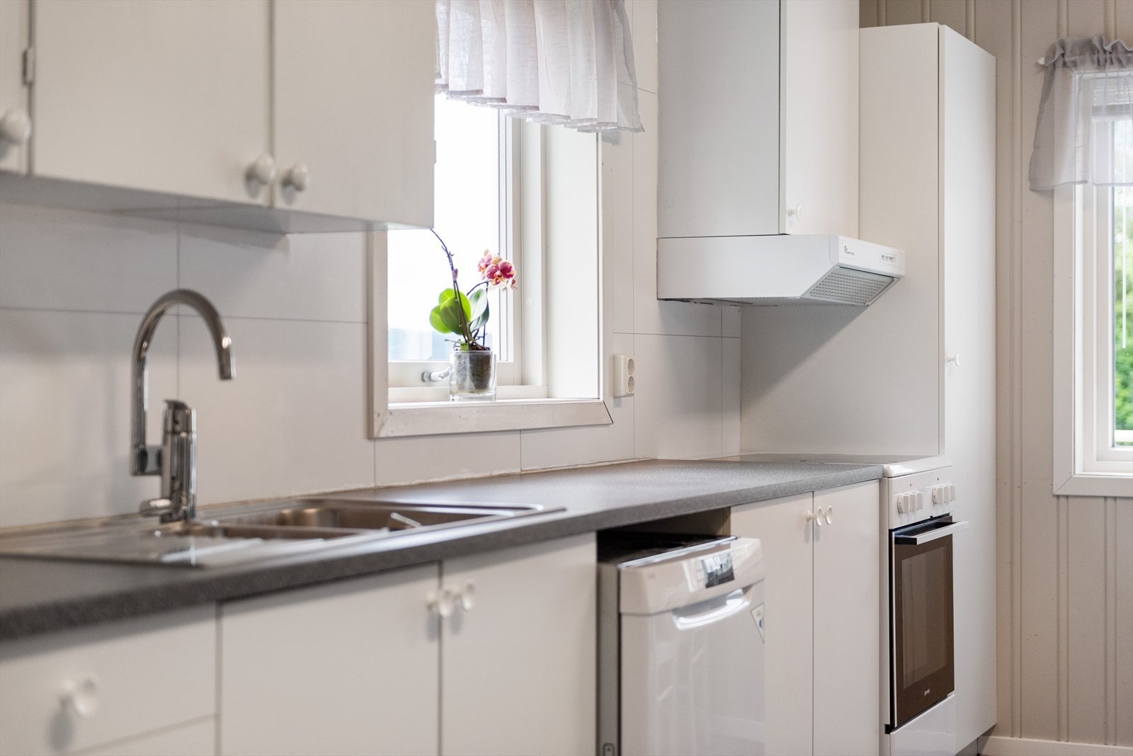 Lys og tidløs kjøkkeninnredning med hvite glatte fronter og laminert benkeplate med nedfelt oppvaskkum. Praktisk med plater i benkeryggen og belysning under overskapene. Galleribilde