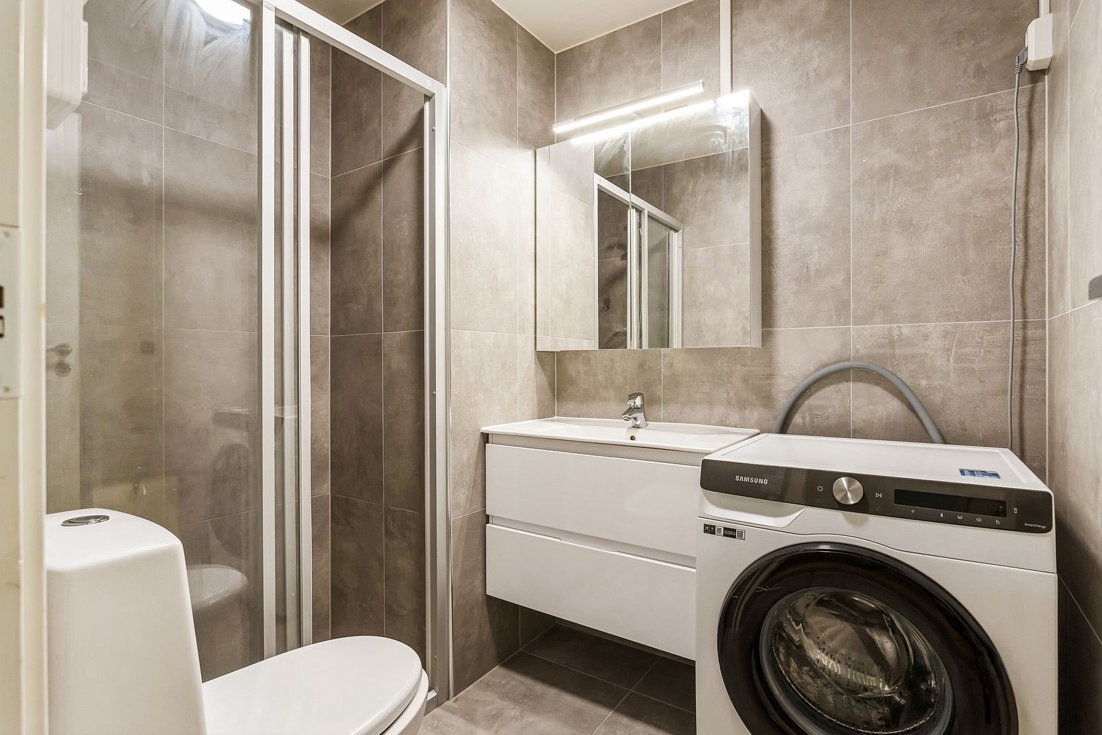 Badet er helfliset med dusj, toalett, servant, speil og vaskemaskin Galleribilde