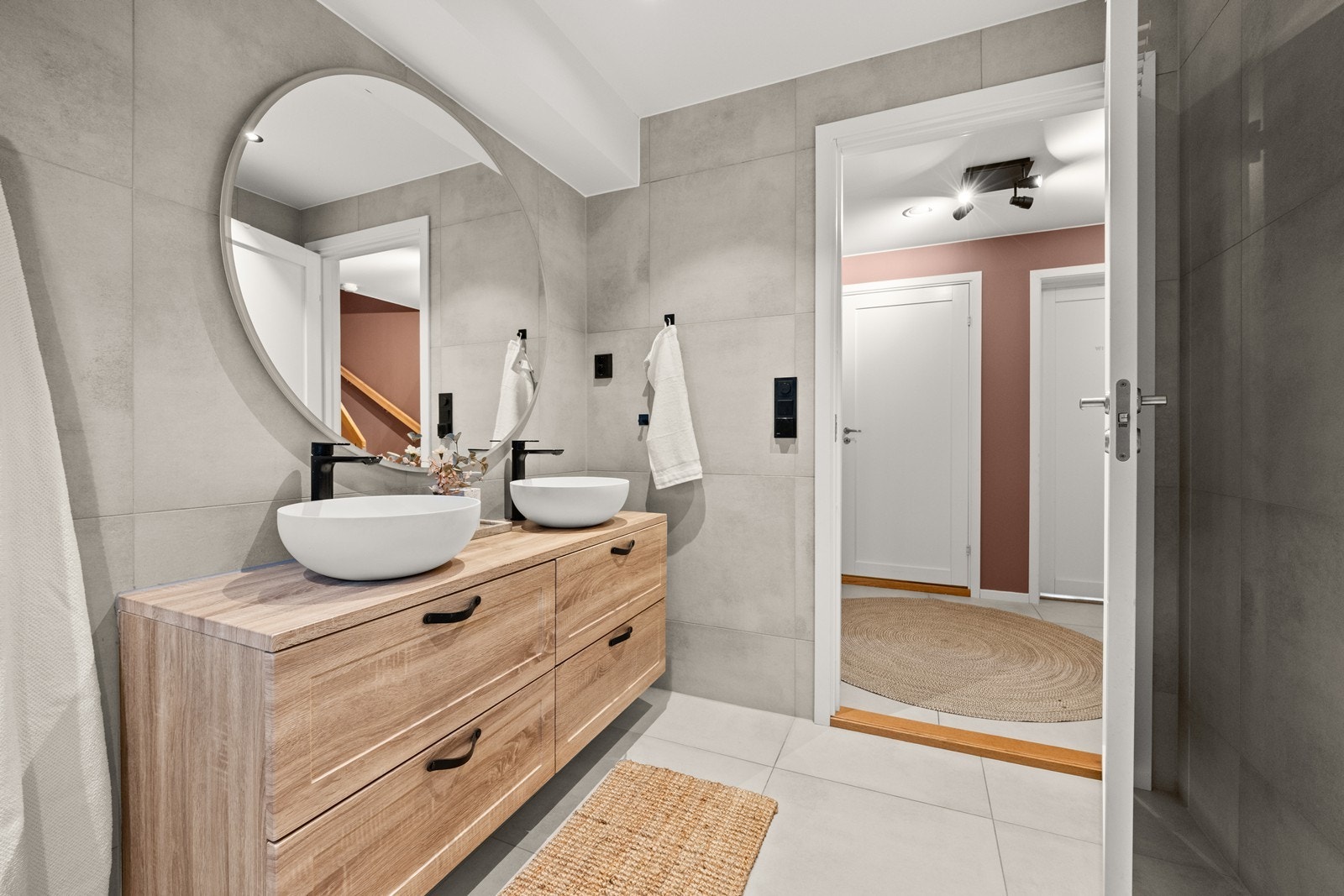 Badet er utstyrt med dobbelt servantskap med servantboller, speil med lys, dusnisje med innfellbare dører og regndusj, og vegghengt toalett Galleribilde