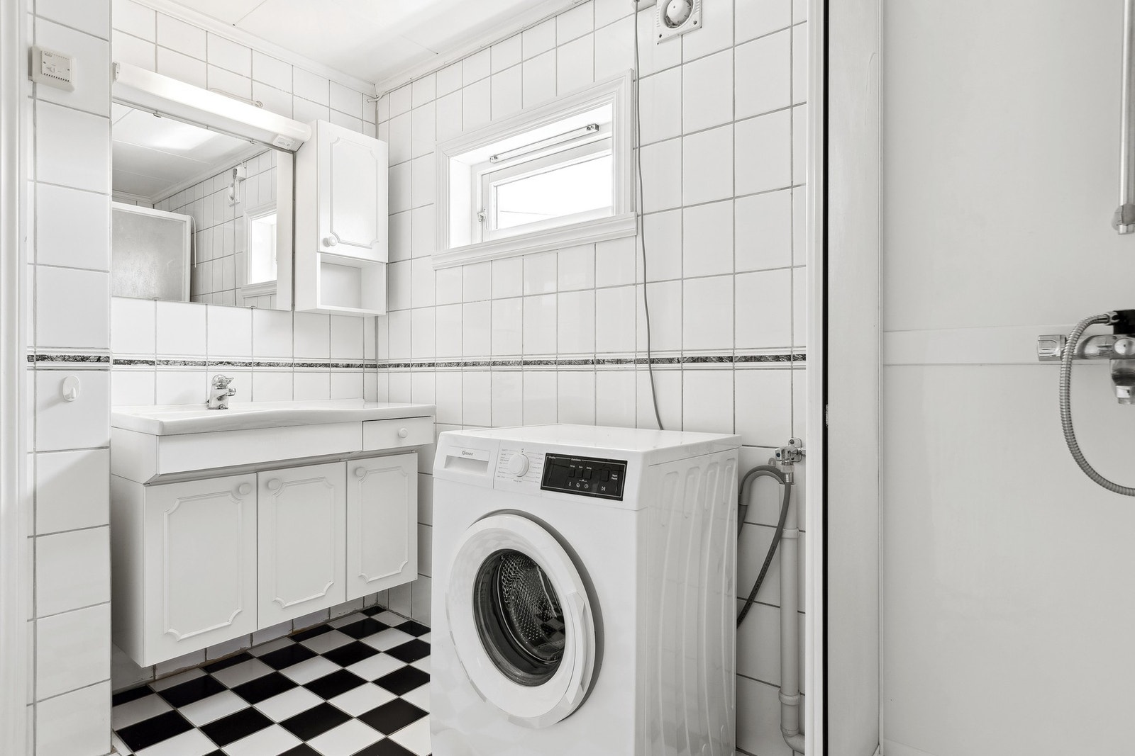 Lyst flislagt bad med servantinnredning, praktisk dusjkabinett og opplegg for vaskemaskin. Galleribilde