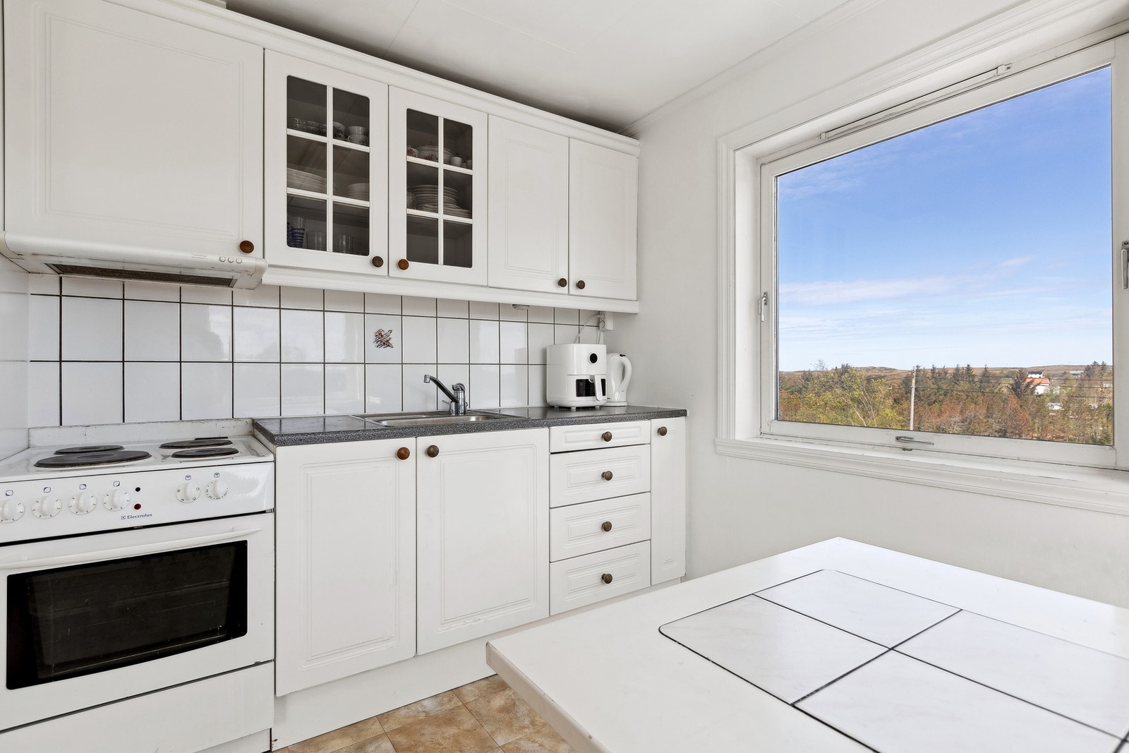 Kjøkkeninnredning med profilerte fronter, laminat benkeplater og nedfelt benkebeslag i rustfritt stål. Avtrekkshette over stekesone. Galleribilde