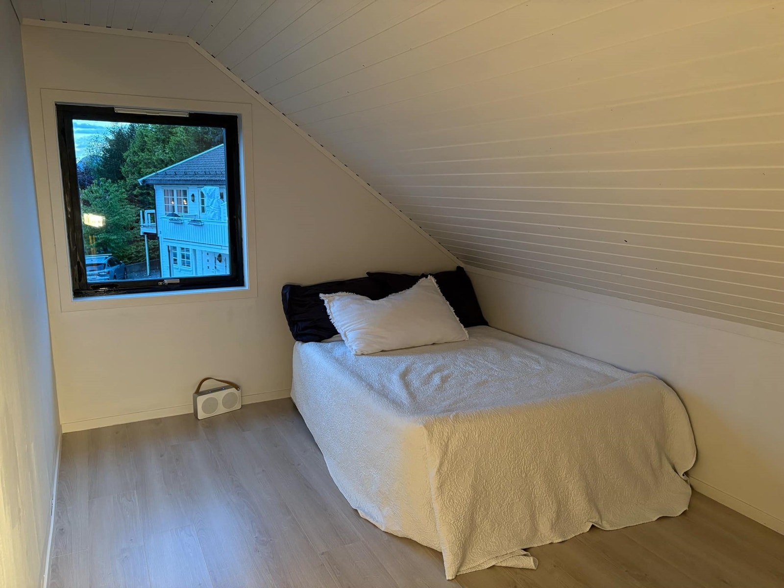 Lyst og koselig soverom med skråtak. Stort vindu gir naturlig lys og utsikt mot frodig natur. Rolig atmosfære. Galleribilde