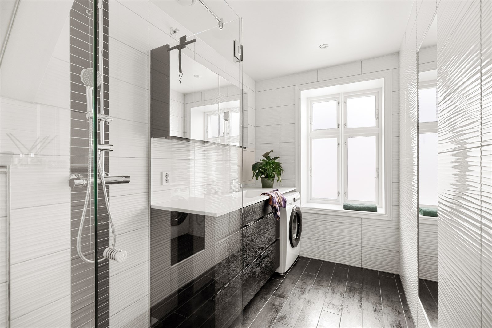 Badet er innredet med sort vask i seksjon og speilskap på vegg, vegghengt toalett og dusjhjørne i klart glass. Galleribilde