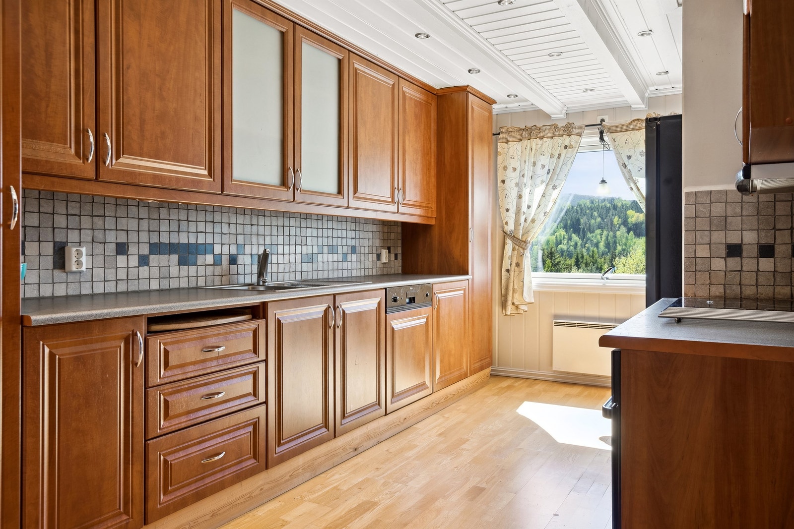 Rikholdig innredning, med integrert stekeovn, induksjonstopp og oppvaskmaskin. Fliser over benk. Downlights. Galleribilde