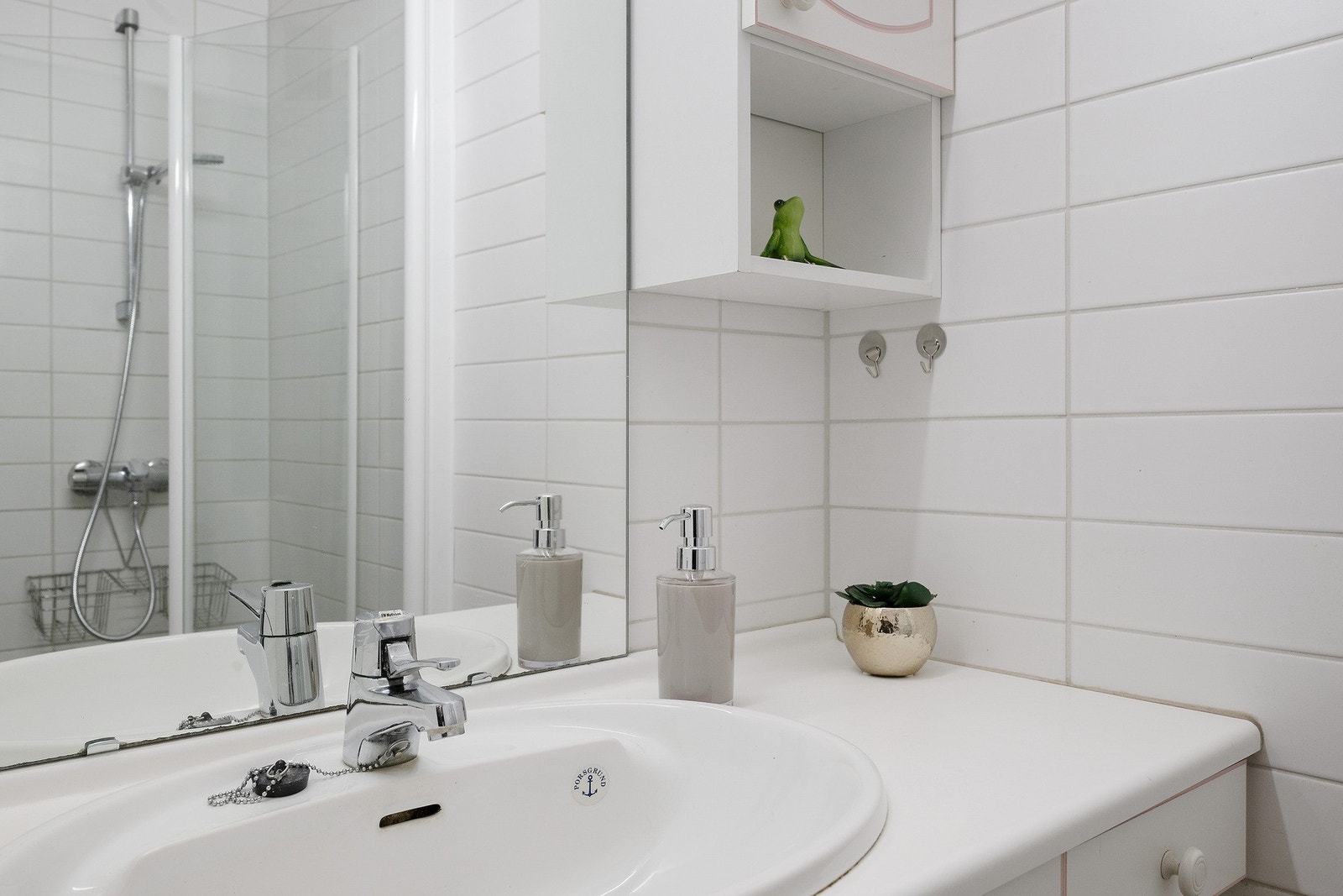 Baderomsinnredningen har hvite, profilerte fronter og består av en nedfelt servant på en skapløsning, et høyskap, veggskap og speil med belysning. Videre har badet et toalett og et dusjhjørne med glassdører. Galleribilde