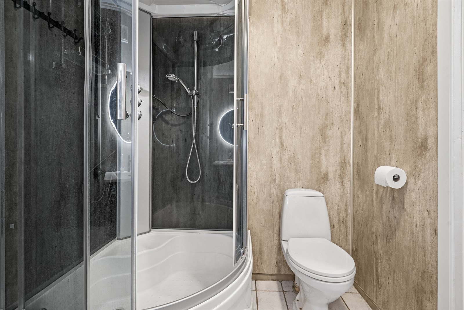 Badet er utstyrt med toalett og dusjkabinett, og har flislagt gulv. Galleribilde