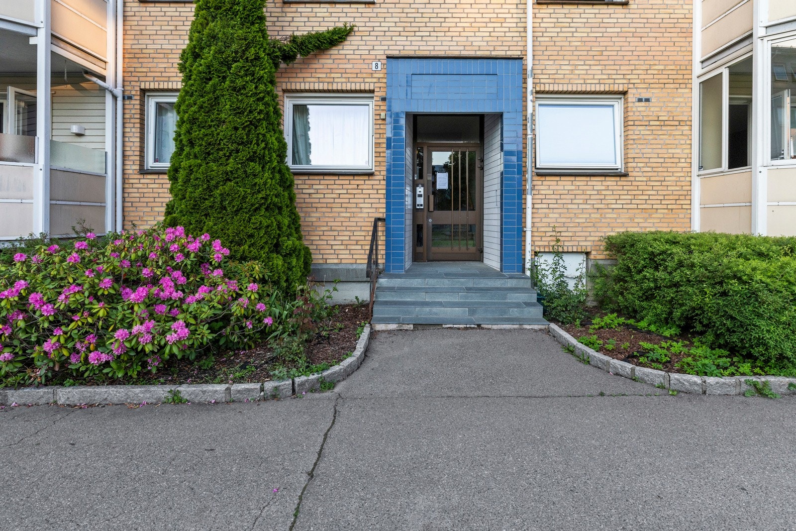 Bygget har en koselig felles inngang, dekorert med blomster og buskevekster Galleribilde