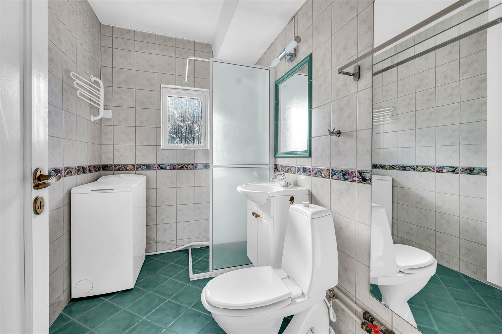 Fra gangen er det inngang til et flislagt baderom med gulvvarme. Rommet holder en eldre standard, og renovering bør påregnes før videre bruk. Galleribilde