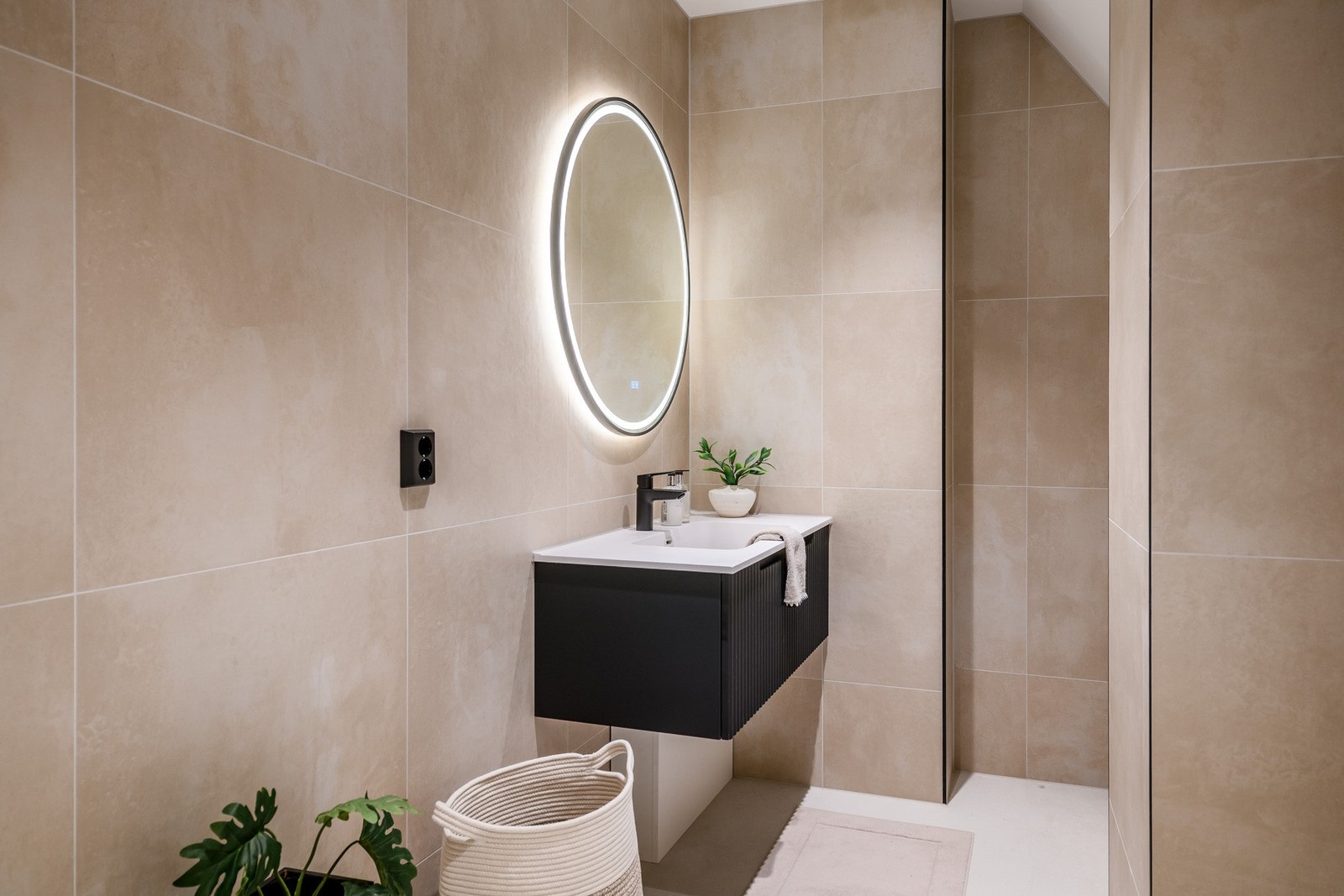 Badet er lekkert med lyse fliser på gulv og vegger, gulvvarme og stilig innredning med sorte detaljer. Galleribilde