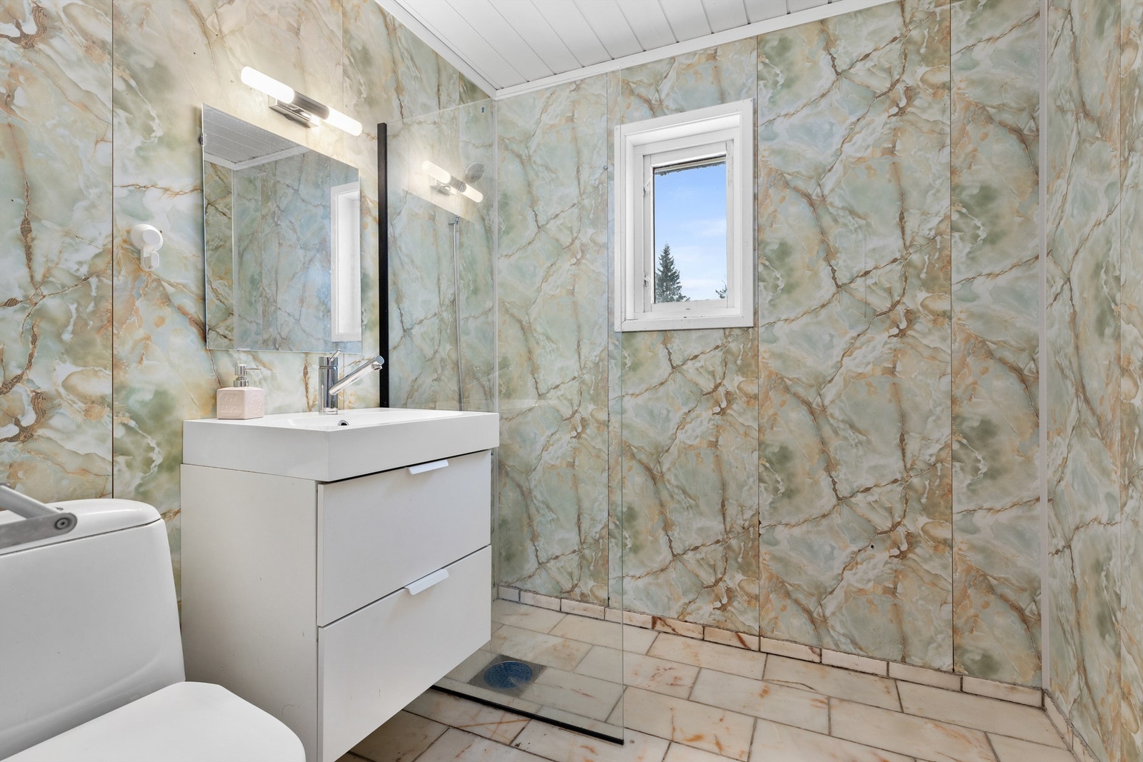 Bad fra byggeår. Flislagt gulv med varme og flislagte vegger. Vegghengt servantskap med ovenpåliggende servant og ett-greps armatur. Speil og belysning over servant. Gulvstående toalett. Dusjhjørne med glassvegg. Galleribilde