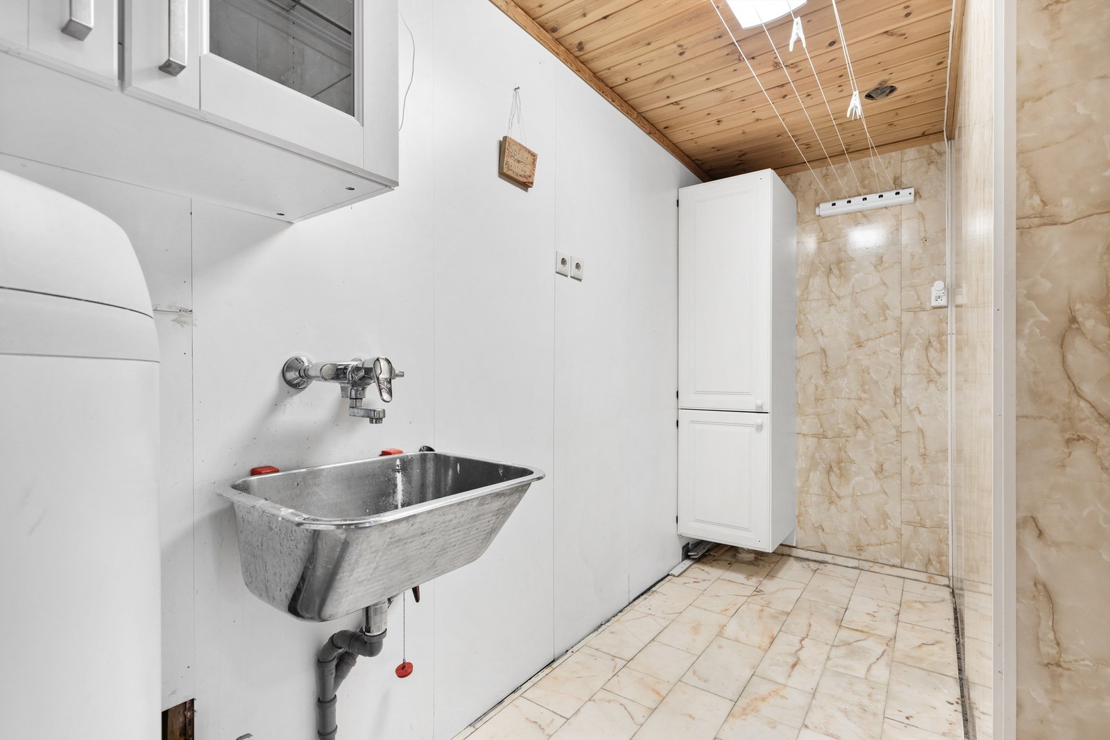 Vaskerom fra byggeår. Flislagt gulv. Våtromsplater på vegger. Himling med panel. Vegghengt utslagsvask med ett-greps armatur. Vannrør av kobber. Avtrekksventil i himling. Opplegg for vaskemaskin. Galleribilde