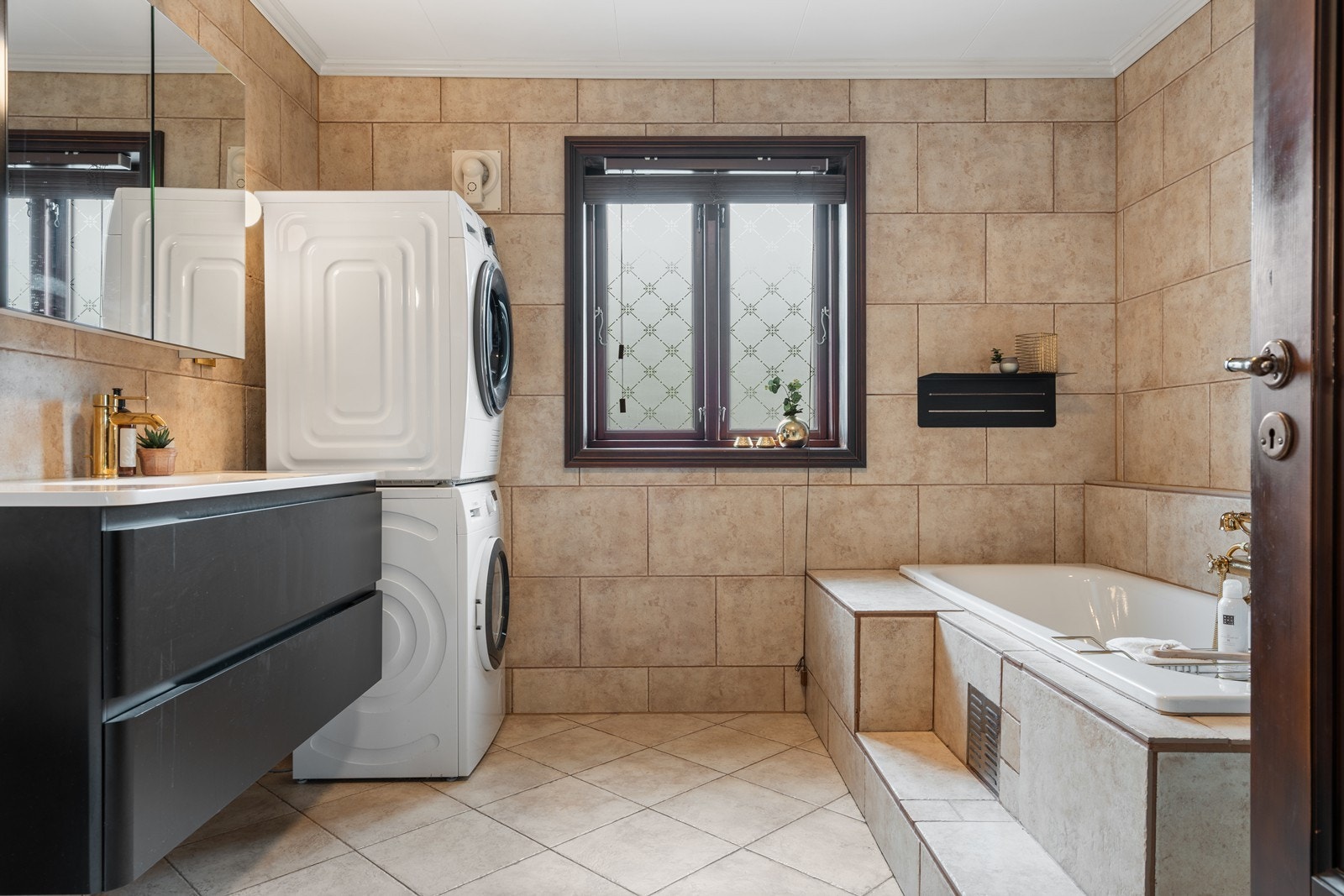 Badet er innredet med sort baderomsinnredning, dusjkabinett, badekar, gulvmontert toalett og opplegg for vaskemaskin Galleribilde