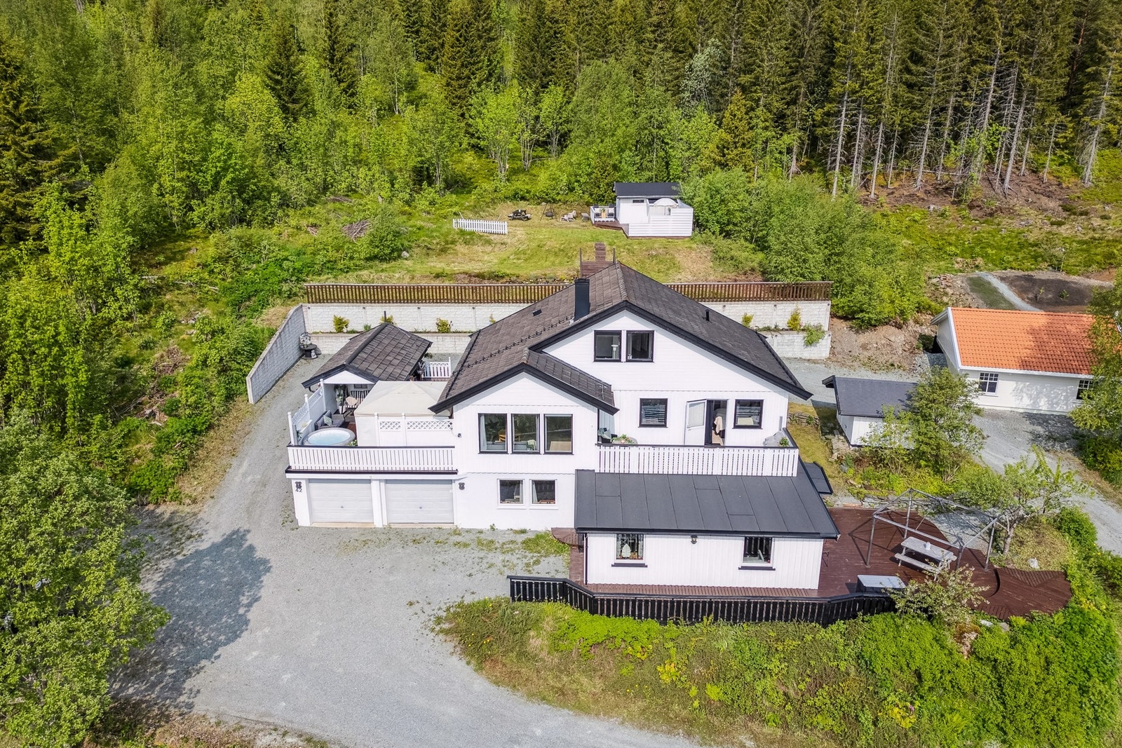 Tomt opparbeidet med grus, diverse beplantninger, plenareal, terrasse på
terreng, støttemurer og biloppstillingsplass. Galleribilde