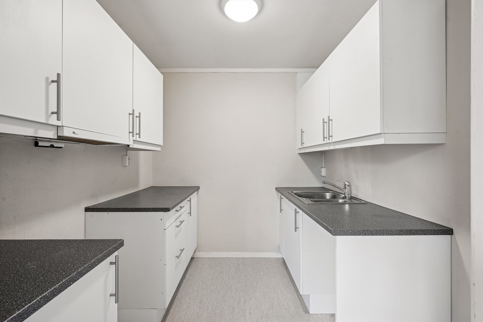 Kjøkkeninnredningen er pent utført med hvite, glatte fronter og mørk laminat benkeplate med nedfelt kjøkkenkum. Galleribilde