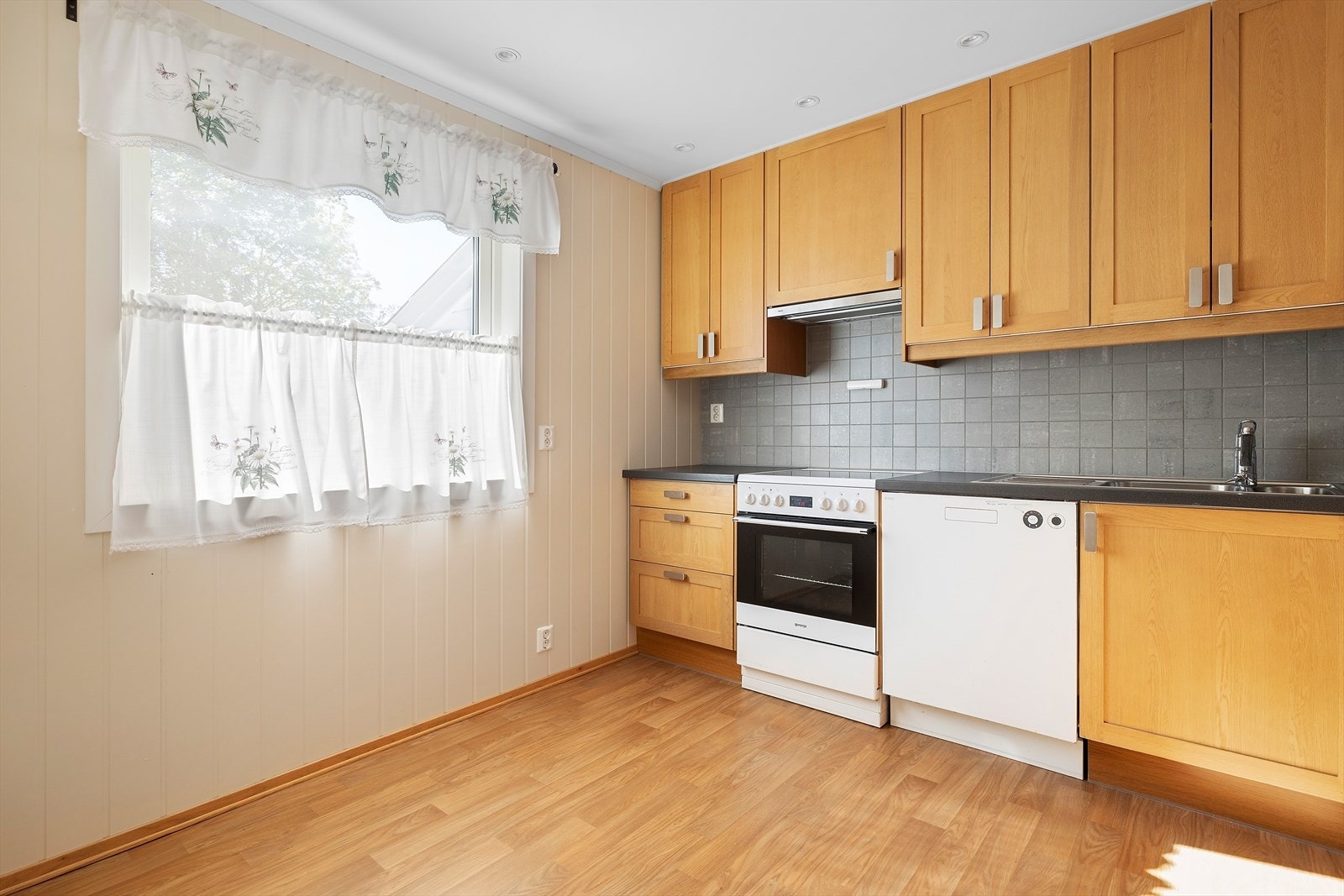 Kjøkkenet har en tidløs innredning med profilerte fronter, laminat benkeplate og fliser mellom benk og overskap. Galleribilde