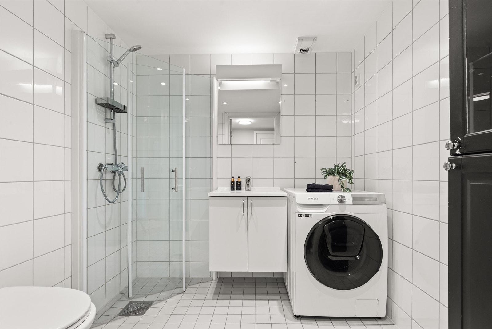 Innredningen består av vegghengt servantskap med ovenpåliggende servant, vegghengt toalett og dusjhjørne med innfellbare glassdører. Badet har lyse fliser på både gulv og vegger samt downlights i himling. Avtrekksventil i himling. Galleribilde