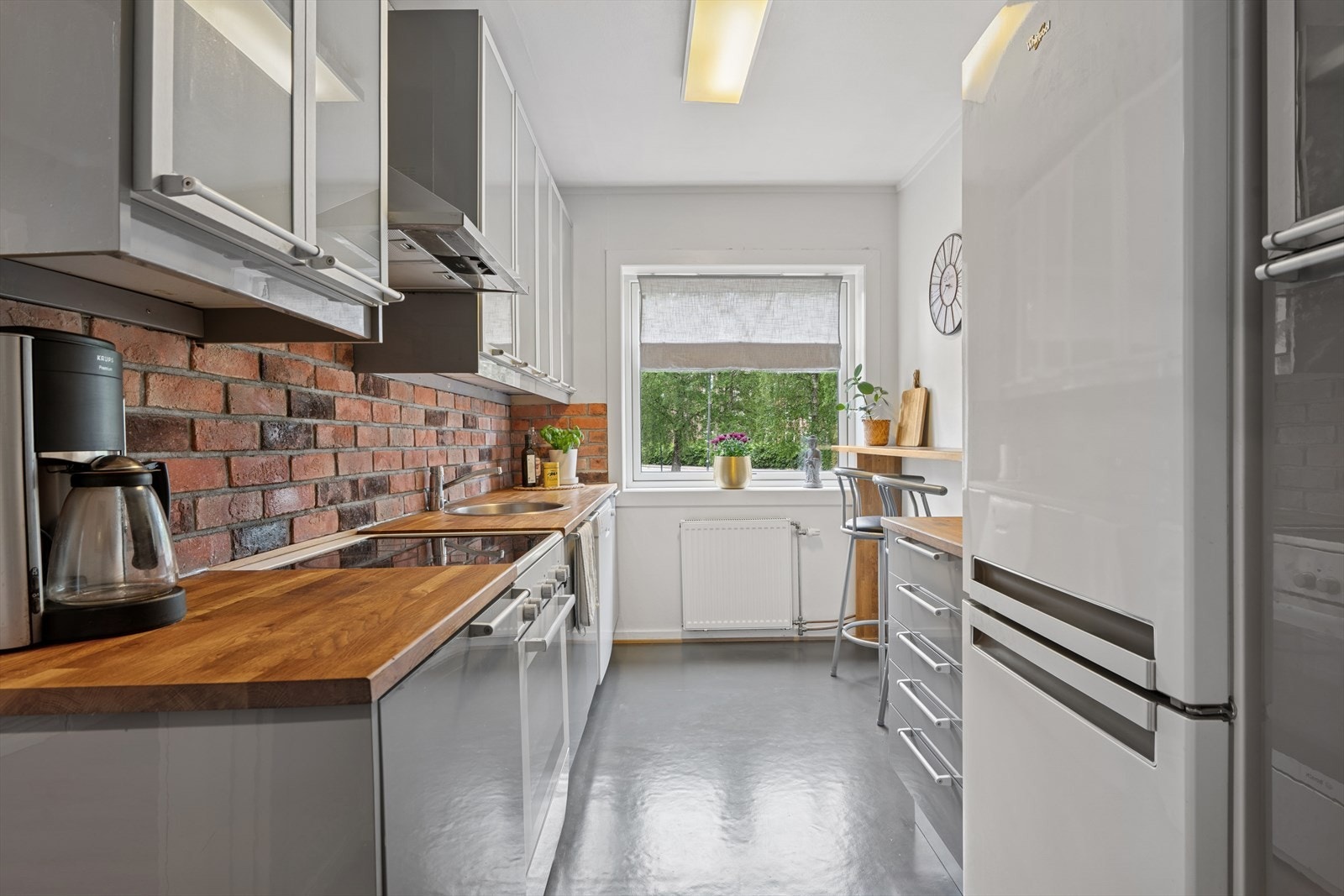 Kjøkkeninnredning med høyglans fronter, benkeplate i tre, oppvaskkum i stål, teglsteinsforblending over benk. Galleribilde