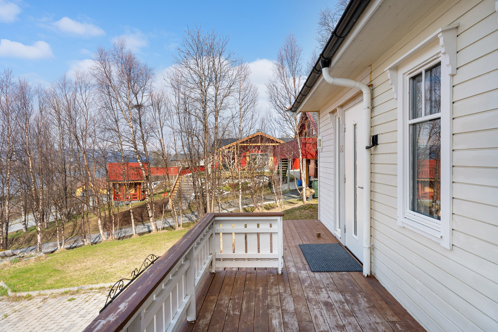 Innbydende inngangsparti med trapp og stor terrasse som strekker seg rundt to sider av boligen