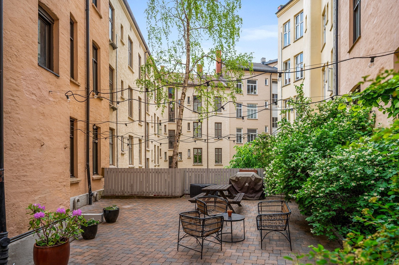 Hyggelig hellelagt gårdsrom med utegrill, sitteplasser og beplantninger. Galleribilde