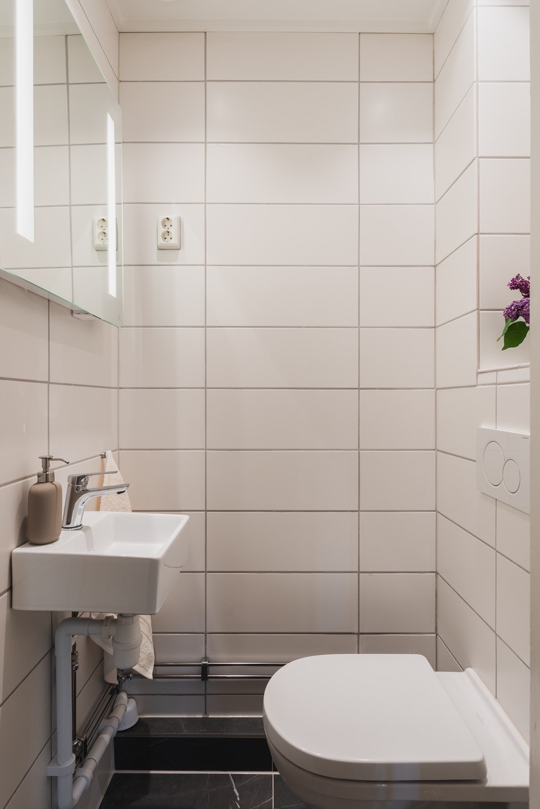 Separat gjestetoalett innredet med vegghengt wc, servant og speil med lys, tidløse fliser på gulv og vegger, malt flate i himling med downlights Galleribilde