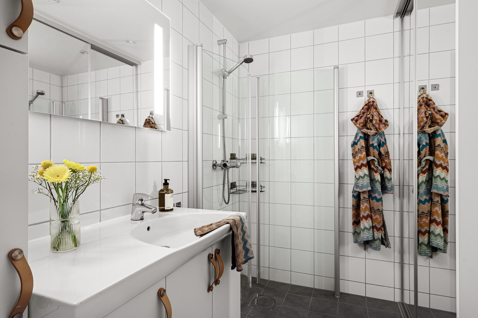 Rommet er innredet med en dusjnisje med glassdører, vegghengt toalett, vask nedfelt i baderomsinnredningen og opplegg til vaskemaskin. Galleribilde