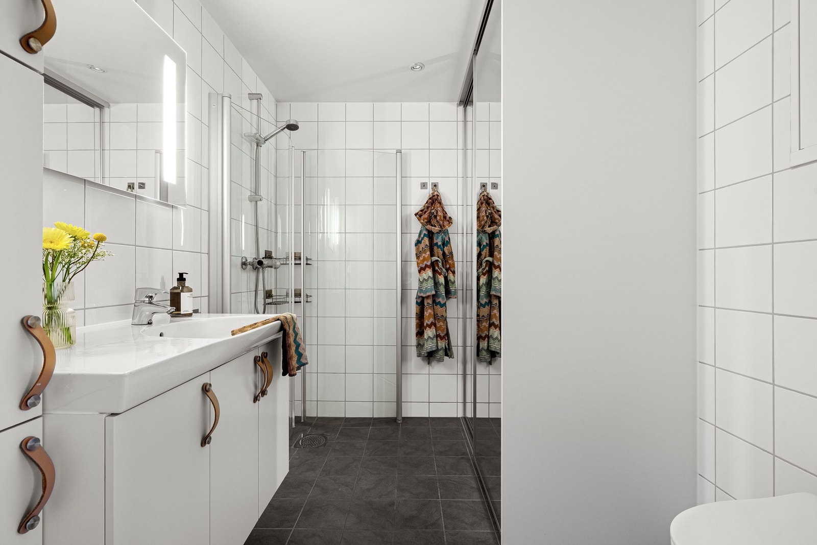 Baderommet oppleves som delikat og stilrent. Her er det mørke fliser på gulvet og lyser fliser på veggene. Varmekabler i gulvet, downlights i tak. Galleribilde