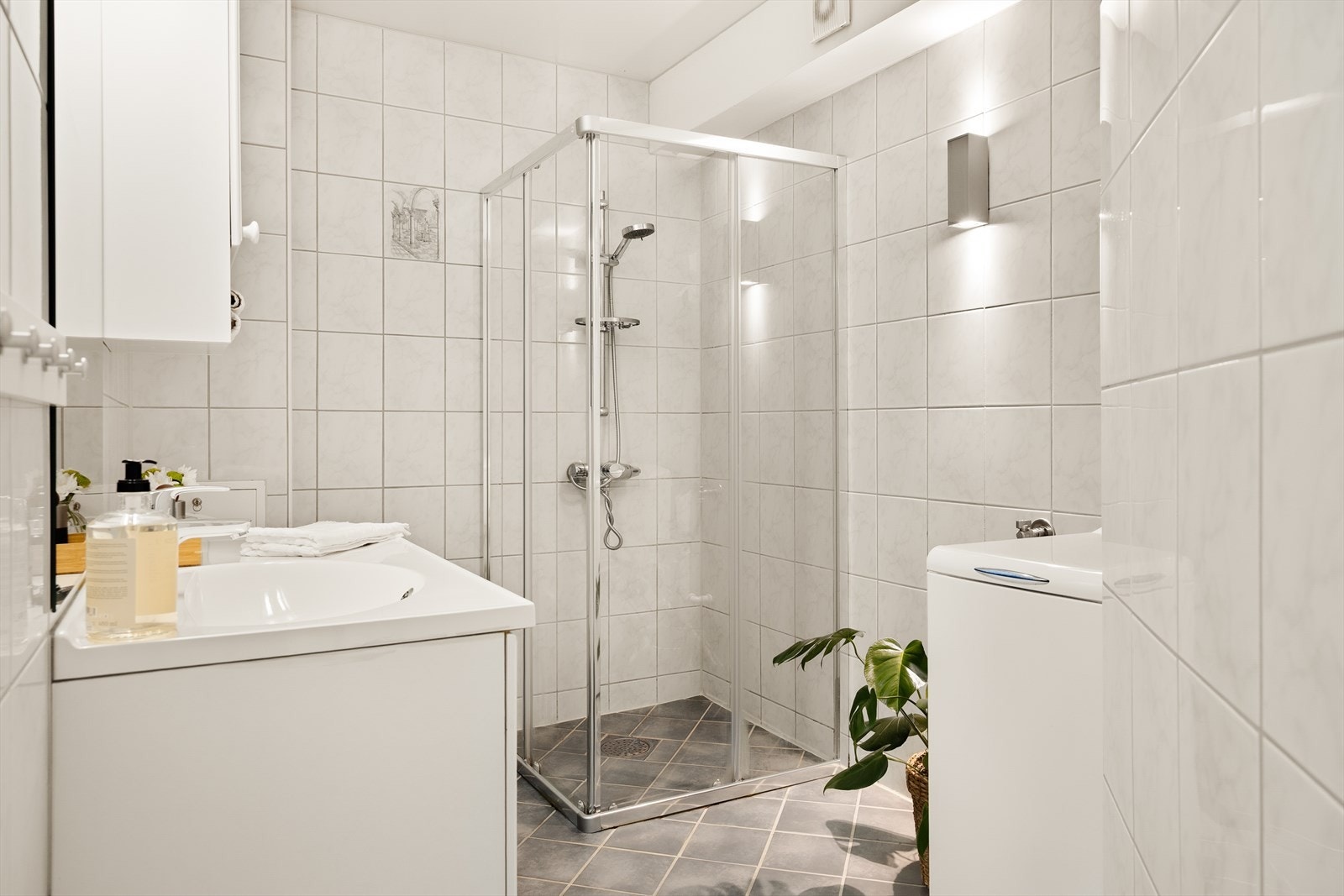 Badet har flislagte gulv med varmekabler og inneholder toalett (skiftet i 2024), helstøpt servant med skuffer under og profilerte fronter, samt dusjdører i klart glass. Det er også opplegg for vaskemaskin. Galleribilde