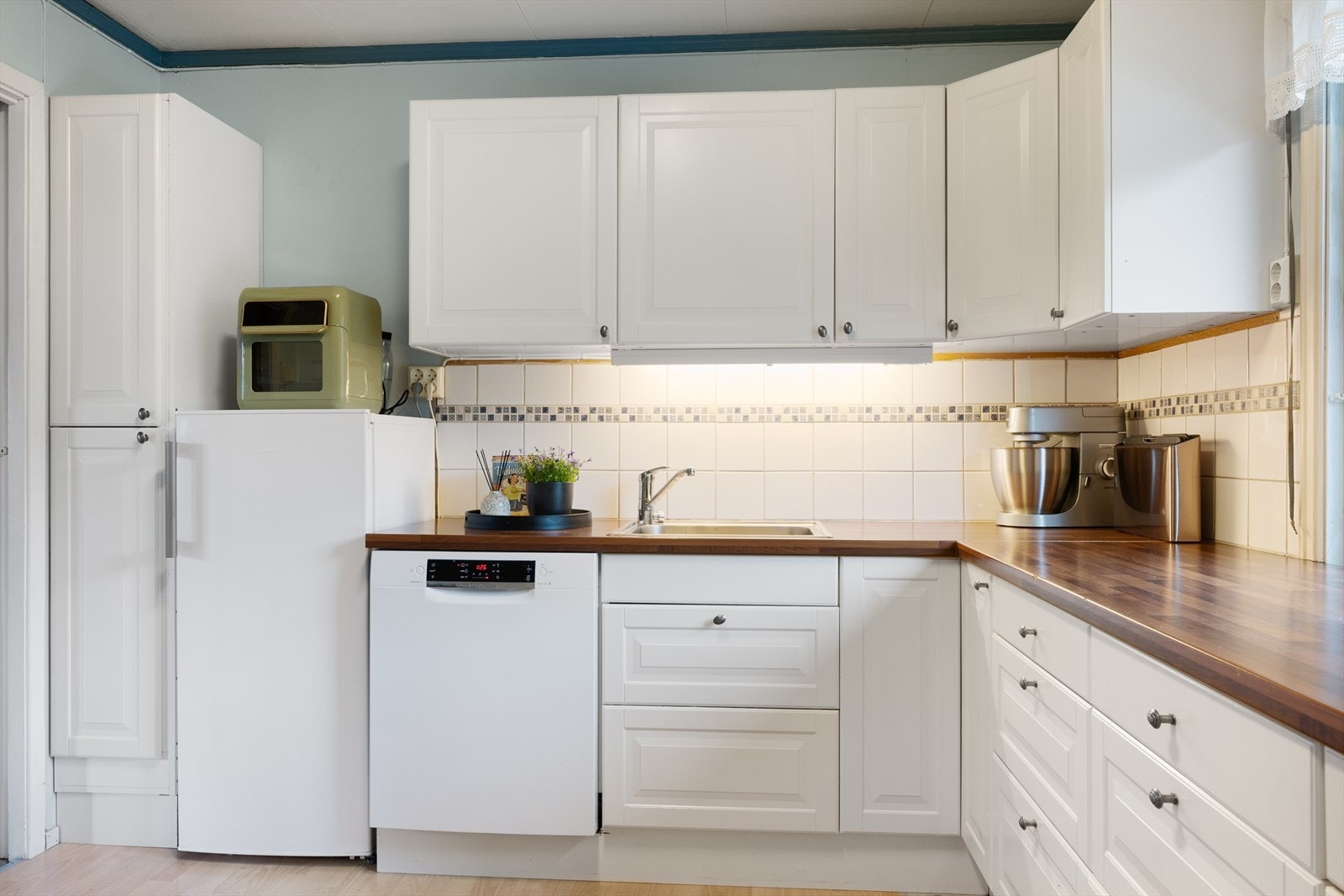 Over kjøkkenbenk er det lagt lyse fliser. Galleribilde