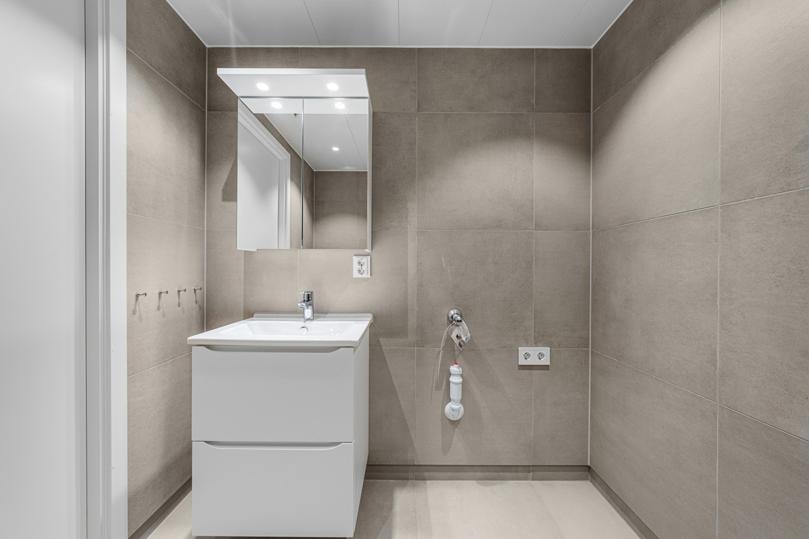 Badet er innredet med dusjhjørne, vegghengt toalett, servant på skuffeseksjon og opplegg for vaskemaskin. Galleribilde