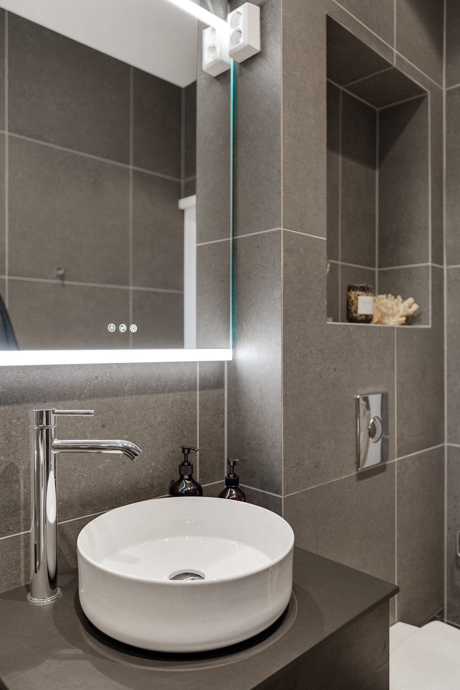 Badet inneholder vegghengt innredning fra 2023 med ovenpåliggende servant, speil med overlys, vegghengt toalett og dusjhjørne med innfellbare dører. Galleribilde