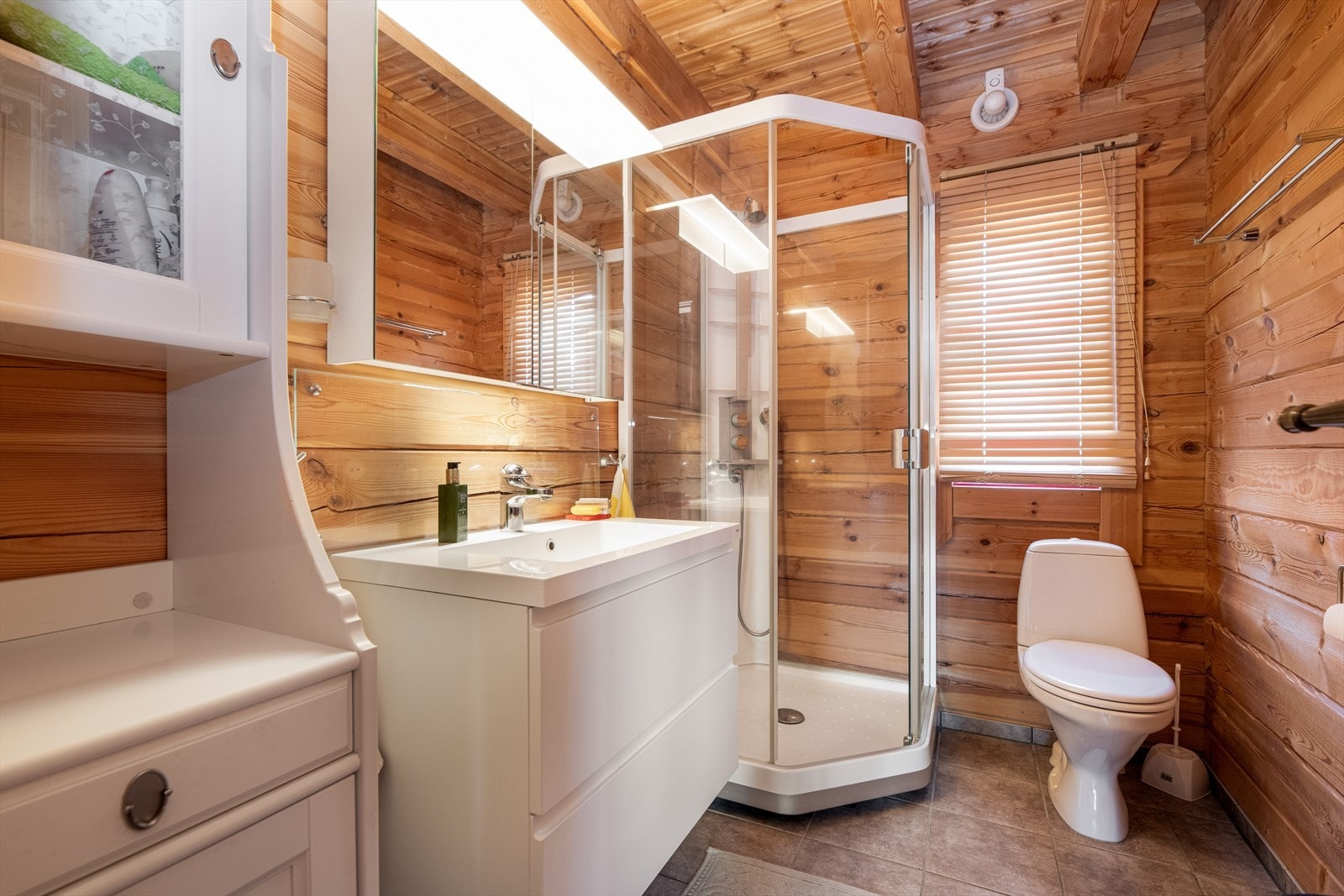 Badet er innredet med toalett, dusjkabinett og servantinnredning med underskuffer og vegghengt skap med speil. Det er varmekabel i gulv. Galleribilde