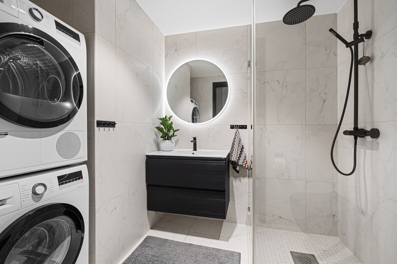 Badet er delikat innredet med moderne 60x60 fliser på gulv og vegger, samt mosaikkfliser i dusjnisjen. Her har du regndusj, vegghengt toalett, baderomsinnredning med speil over, samt egen nisje med plass og opplegg for vaskemaskin/tørketrommel. Galleribilde