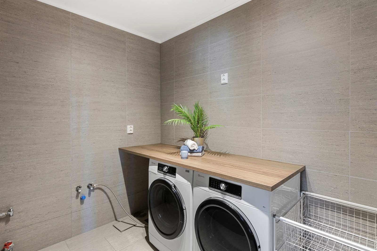 Vaskerom med flis på vegger og malt tak. Flis på gulv og vannbåren gulvvarme. Rommet er innredet med benkeplate og opplegg til
vaskemaskin. Galleribilde