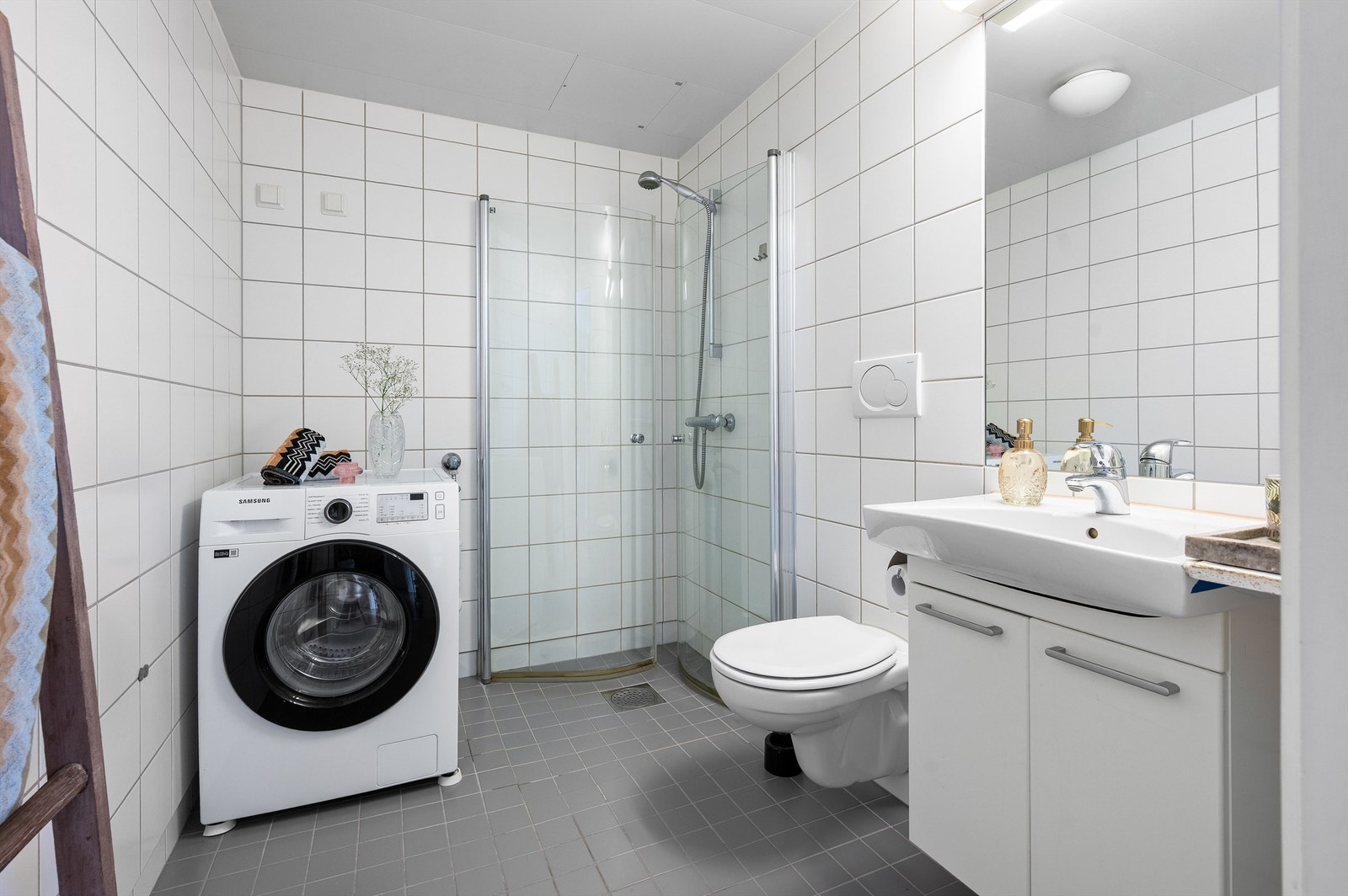 Flislagt bad, med varme i gulv. Badet er innredet med vegghengt servantskap med ovenpåliggende servant, innfliset speil og overlys over servant. Opplegg for vaskemaskin og tørketrommel. Galleribilde