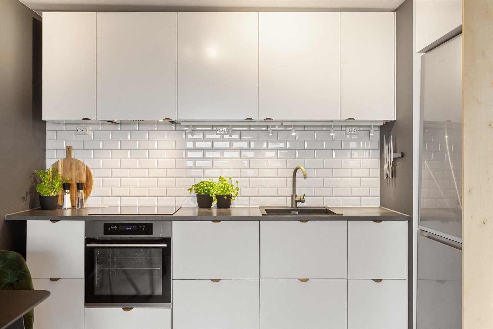 Tidsriktig innredning med glatte, hvite fronter, fliser på vegg over kjøkkenbenk og benkeplate i laminat. Galleribilde