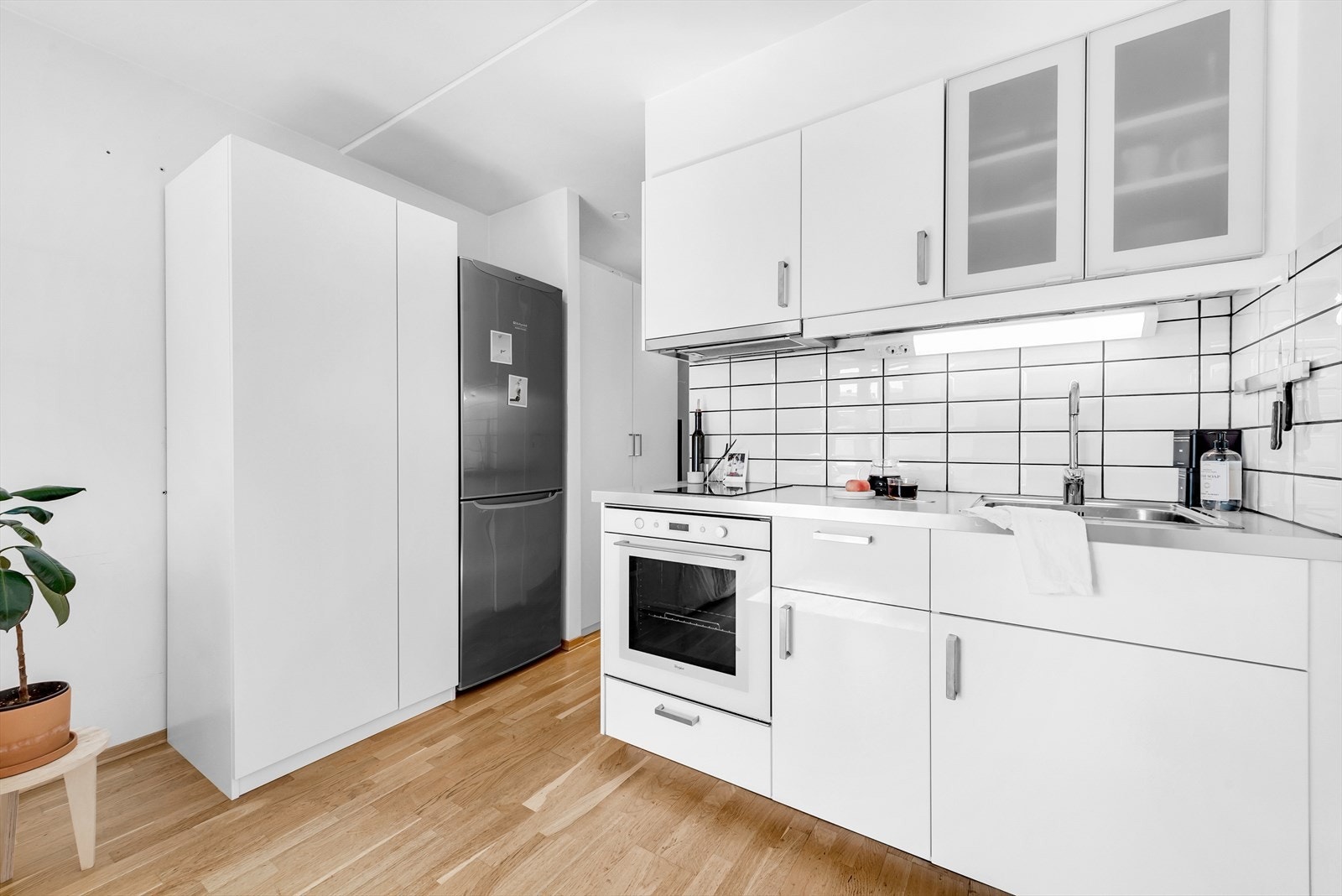 Kjøkkeninnredning med fronter i høyglanset utførelse, enkelte glassfronter i overskap,laminat benkeplate med nedfelt kum i rustfritt stål, fliser på vegg over benkeskap, belysningunder overskap. Galleribilde