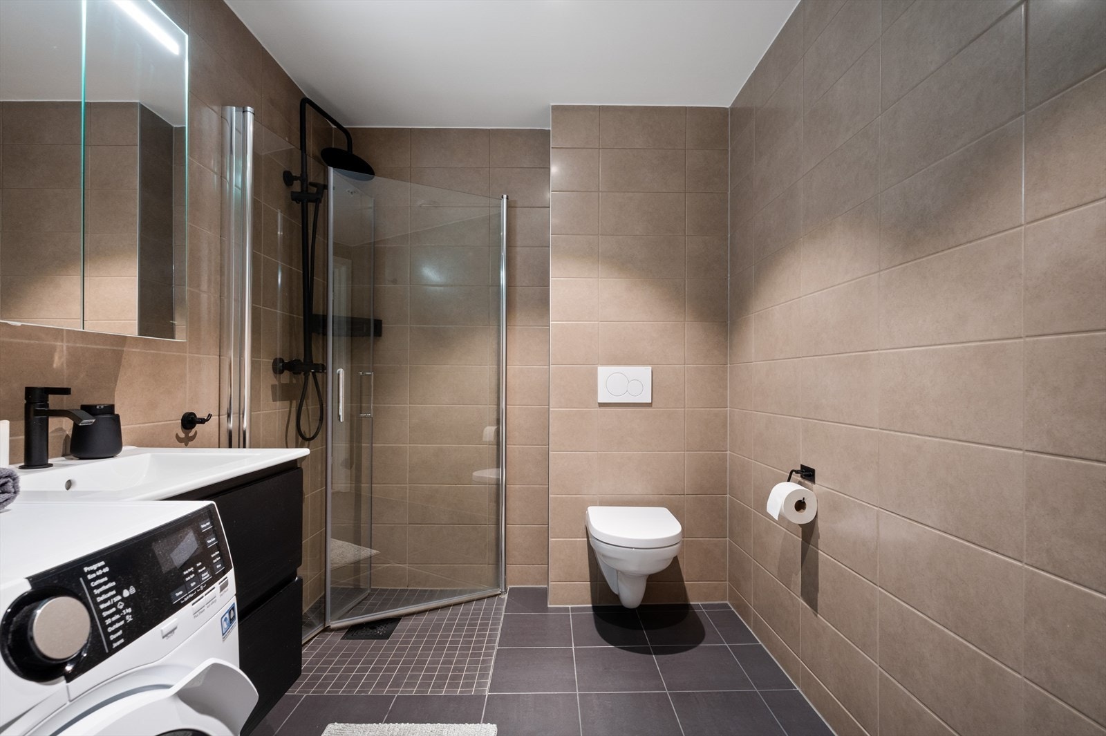 Badet er innredet med baderomsinnredning med servant, vegghengt toalett, dusj og opplegg for vaskemaskin. Galleribilde