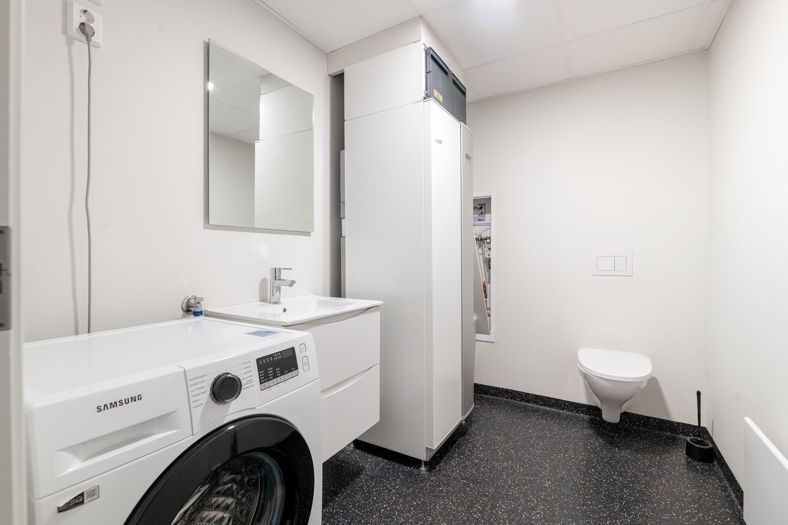 Det er etablert eget vaskerom, med belegg på gulv og malte plater på veggoverflatene, her er det også gulvvarme. Også her er det baderomsinnredning og vegghengt toalett, samt at det er opplegg for og plass til vaskemaskin. Vaskemaskinen medfølger. Galleribilde