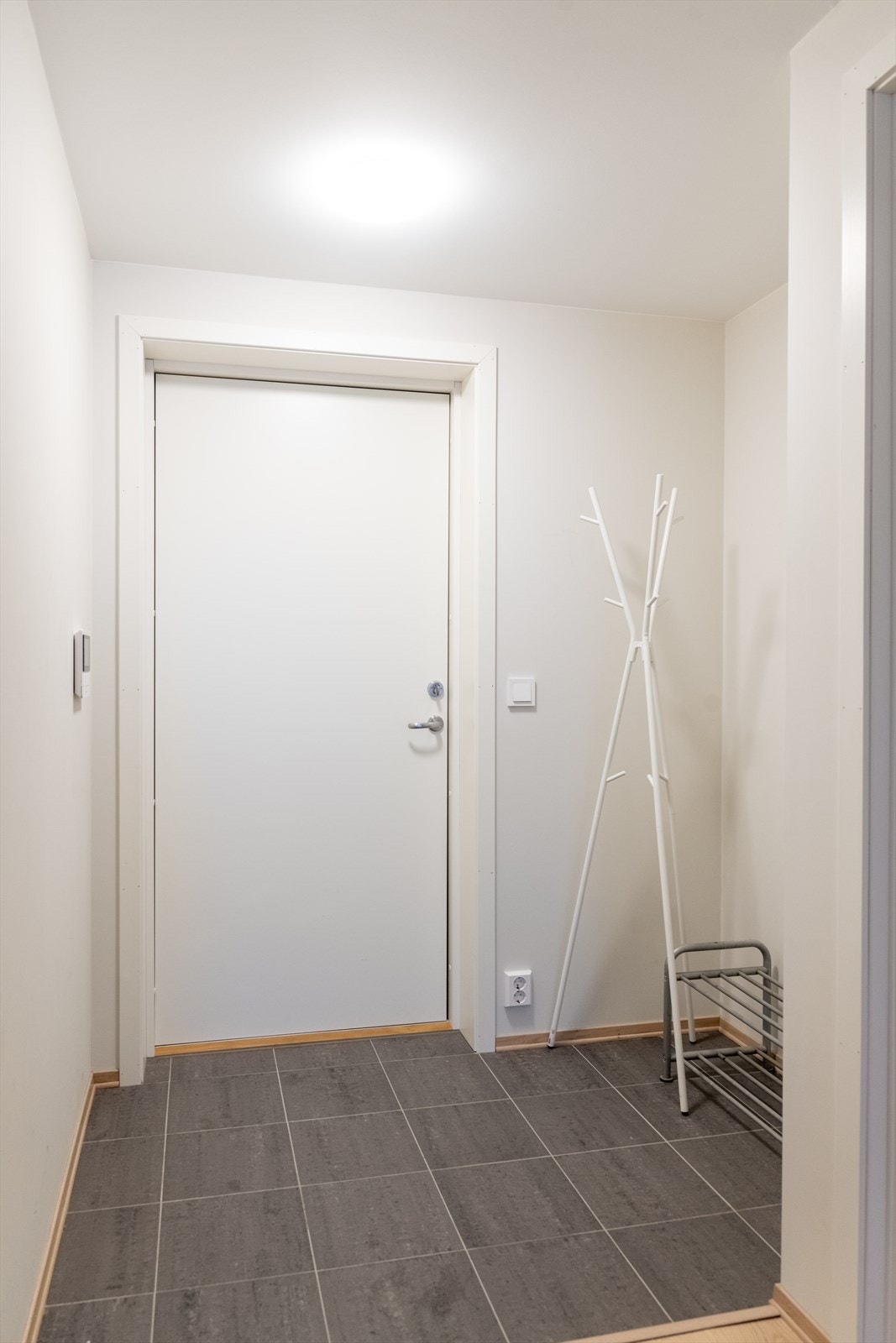 Med adkomst fra svalgangen kommer man inn i gangen, hvor det er flislagt gulv og lysmalte veggoverflater. Her er en liten nisje med plass til sko- og ytterklær, hvor man eventuelt kan sette inn skyvedørsgarderobe om ønskelig. Galleribilde