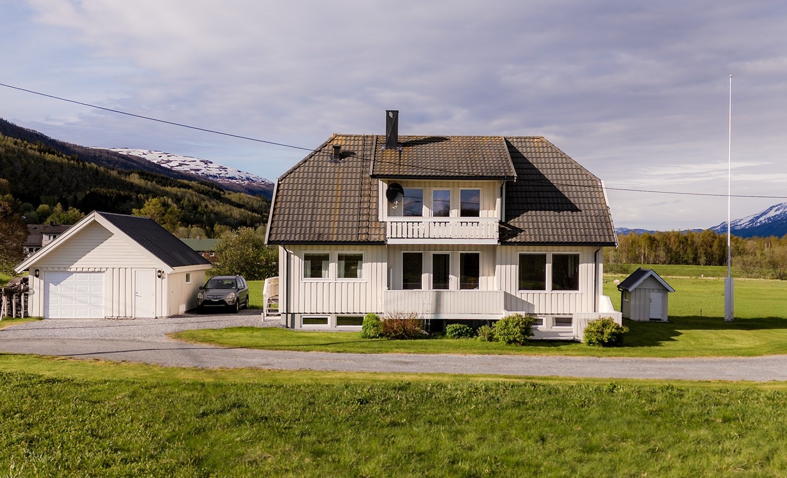 Flat og lettstelt tomt med plen, beplantning og gruset parkering. Galleribilde