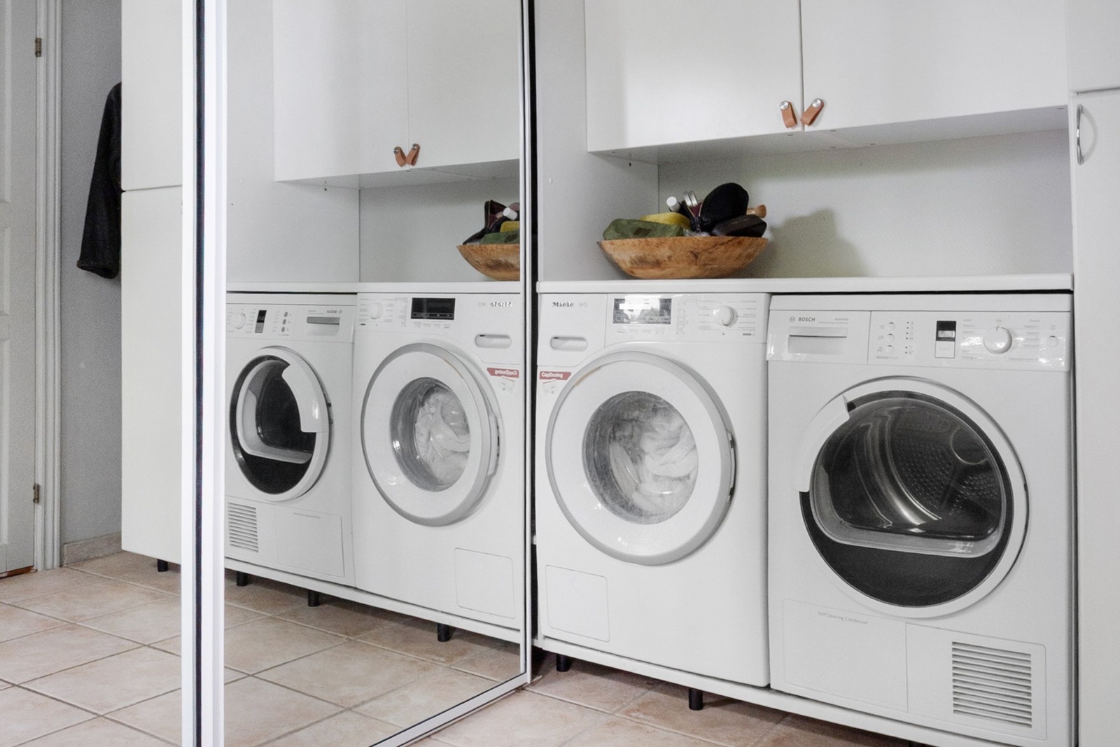 Praktisk vaskerom med fliser på gulv, utslagsvask oppbevaringsplass i skap og skyvedørsgarderobe Galleribilde