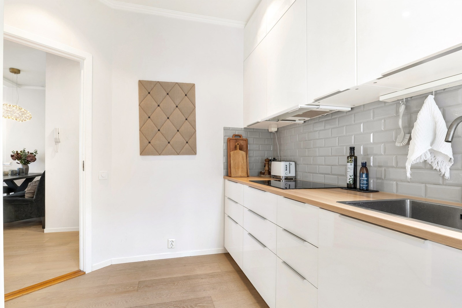 Moderne og tidløst kjøkkeninnredning med hvite glatte fronter og med benkeplate i laminat. Fine grå fliser på vegg over benk og med lys under overskap Galleribilde