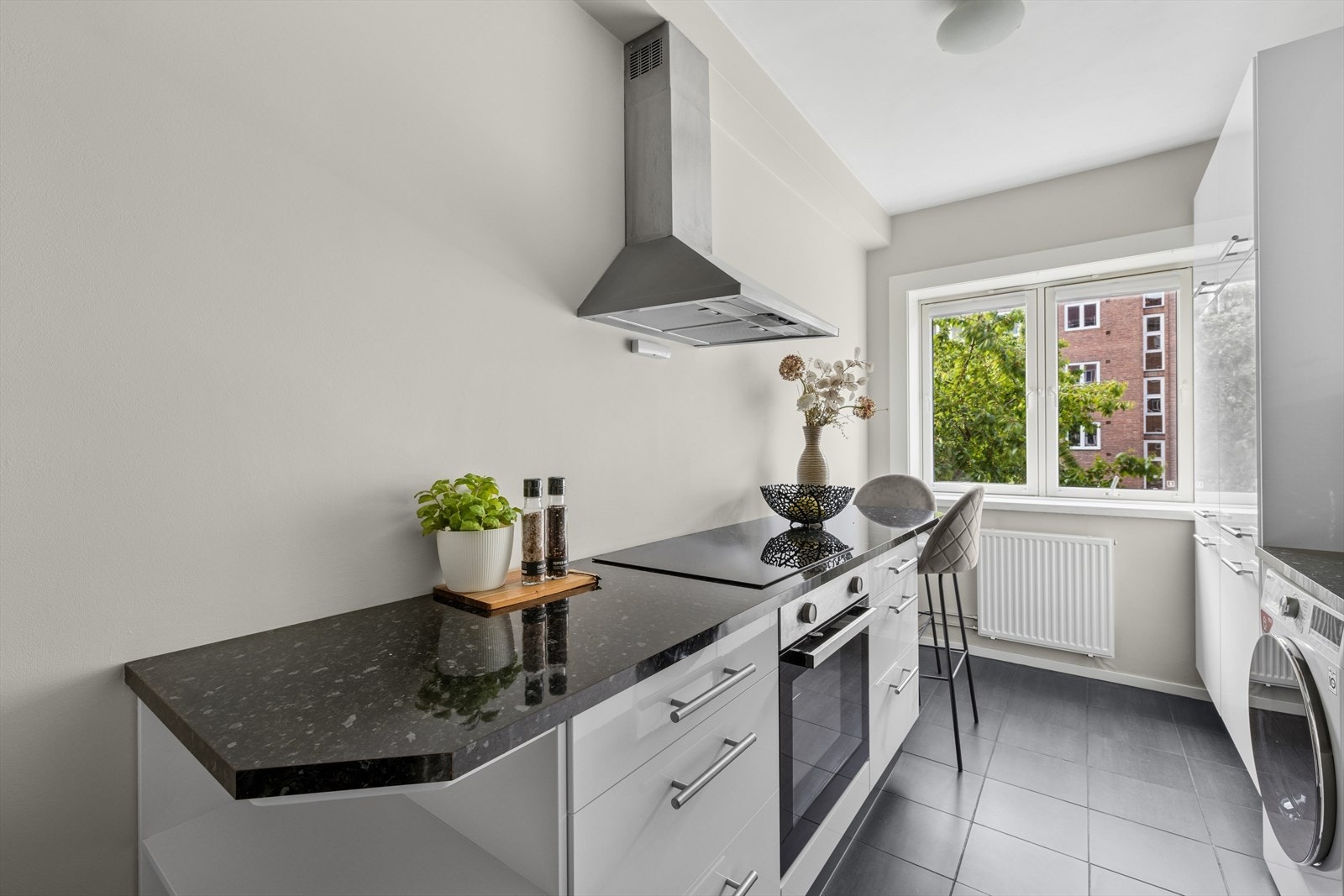 Kjøkkeninnredning med glatte høyglansfolierte fronter, laminat benkeplate med nedfelt kum i rustfritt stål, mosaikkfliser på vegg over benk Galleribilde